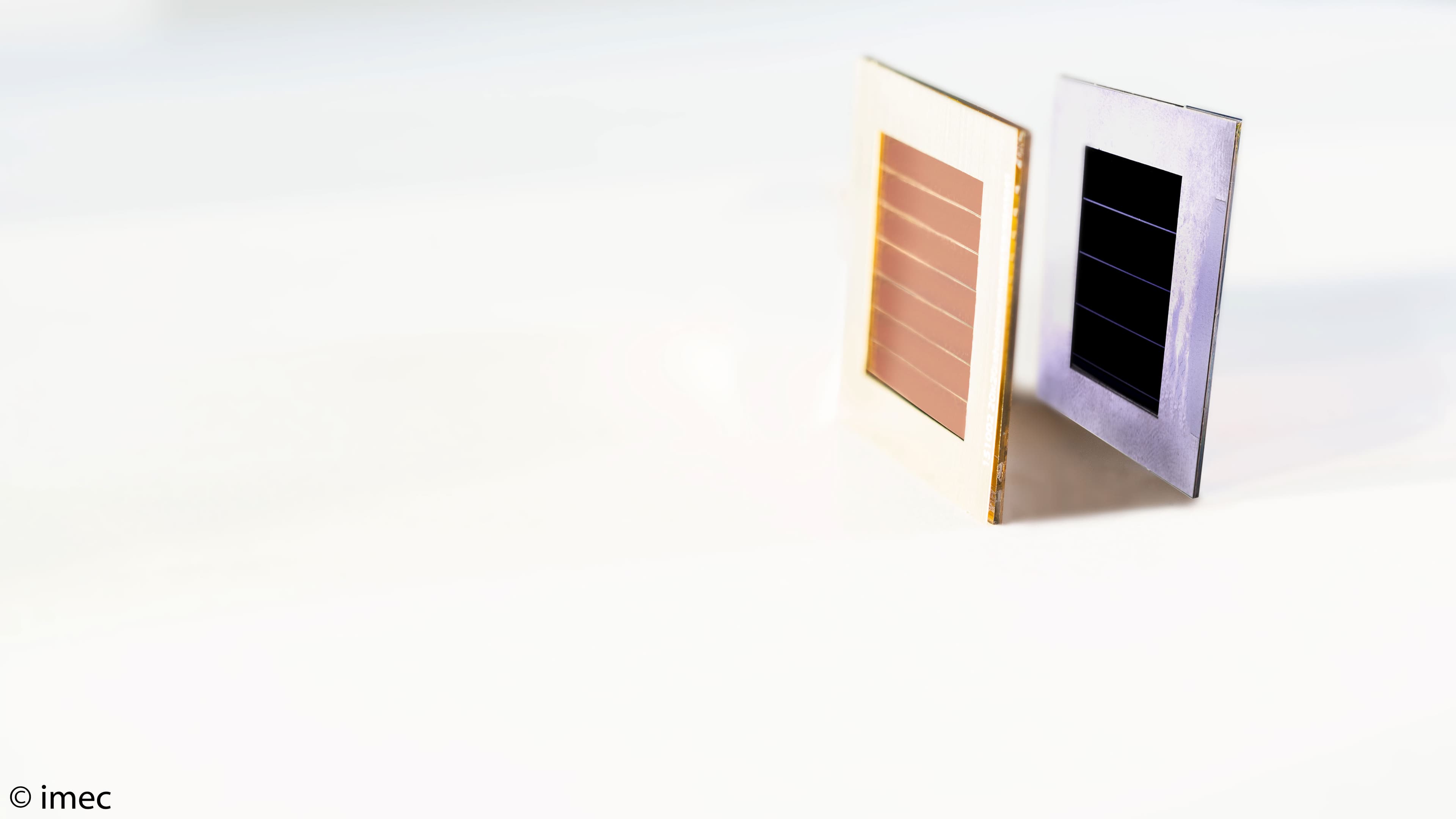 Two thin solar cells suggesting tandem concept Two thin solar cells standing on a white surface, one copper-colored and one dark, suggesting a tandem cell concept.
