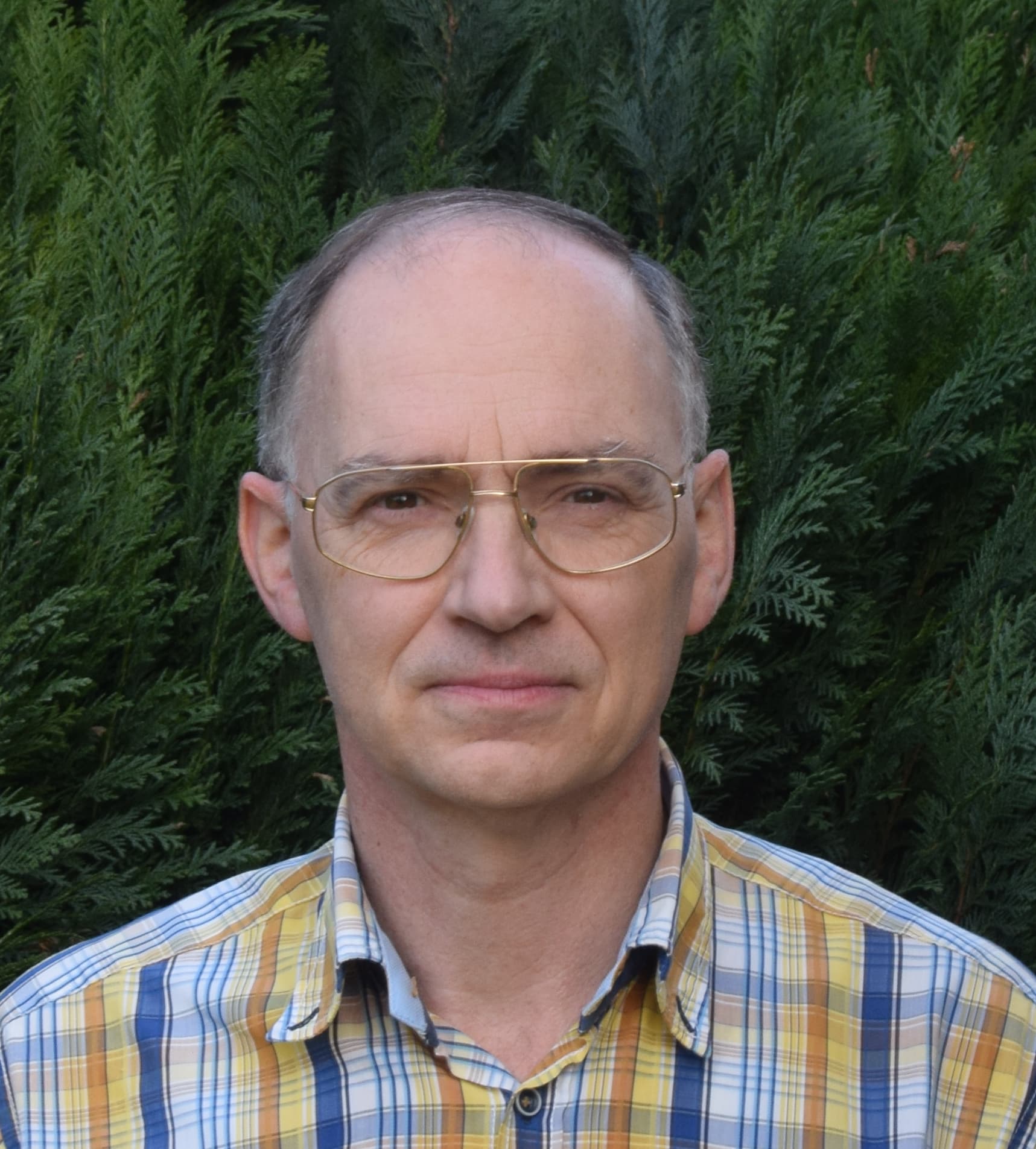 peterdebisschop_1 Portrait of Peter De Bisschop wearing glasses in front of a green hedge