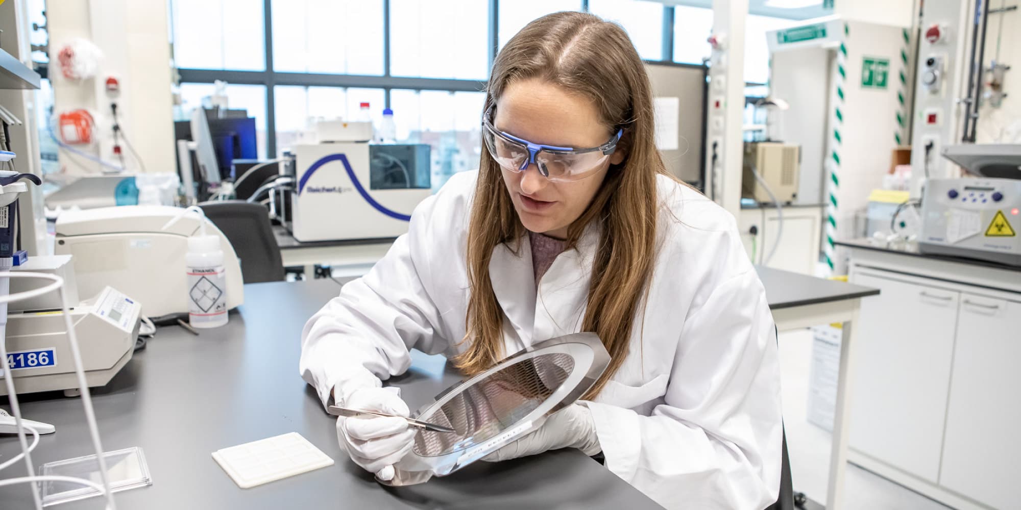 phd-at-imec_0 Researcher in a cleanroom lab examining a silicon wafer with precision tools