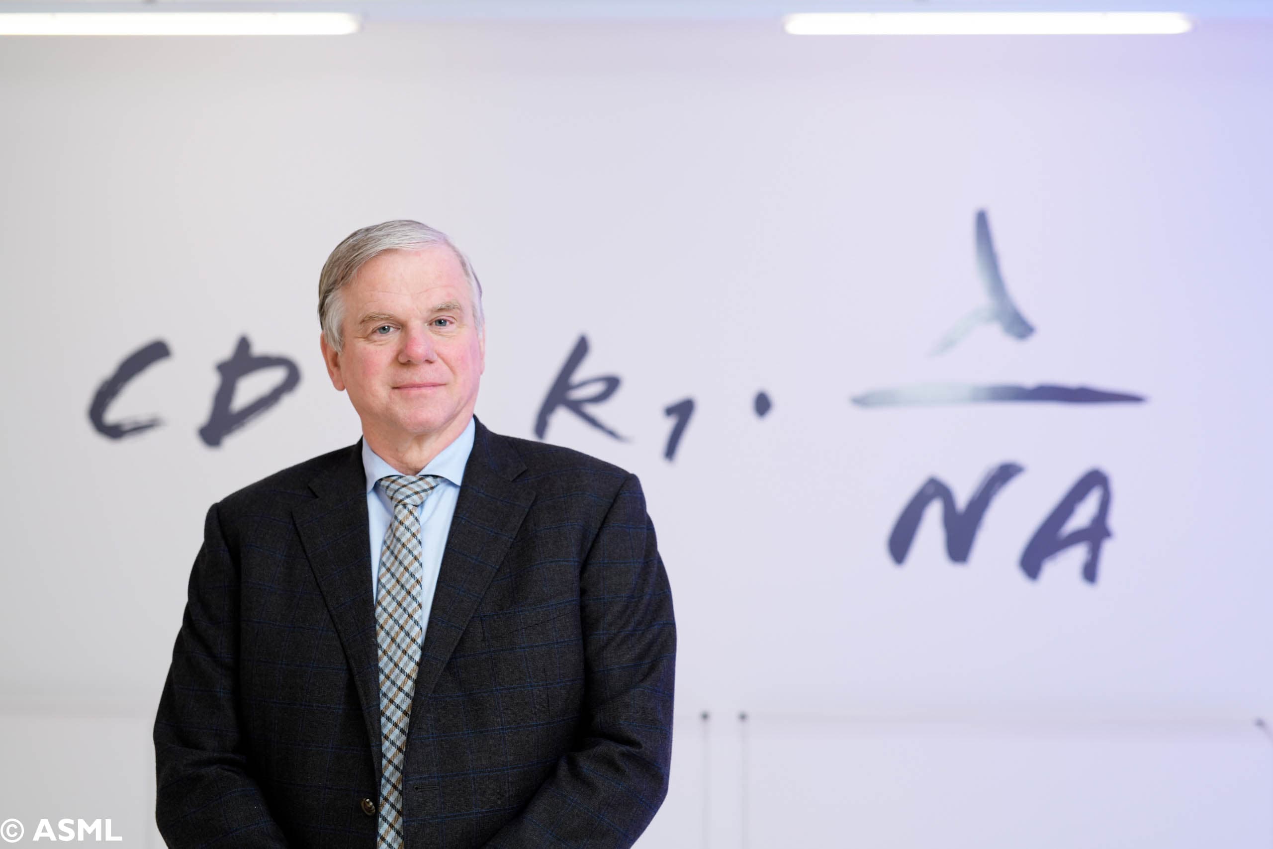 photo_martin-van-denbrink_1 Martin van den Brink in a suit standing before an ASML-branded wall