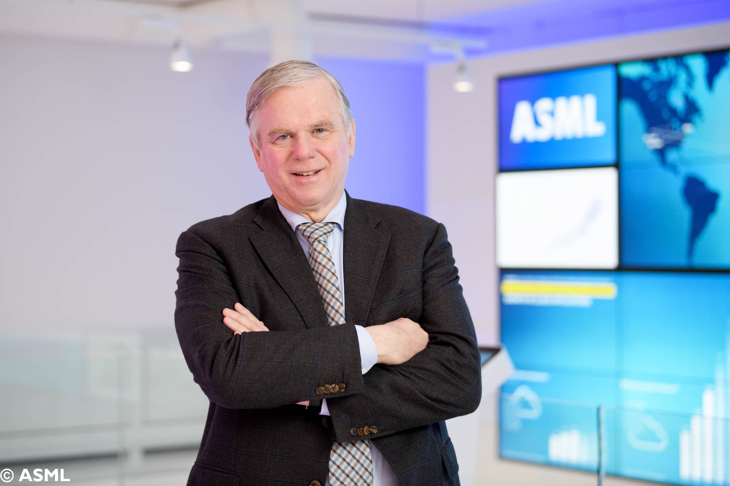 photo_martin-van-denbrink2_1 Martin van den Brink standing with arms crossed in front of an ASML display wall