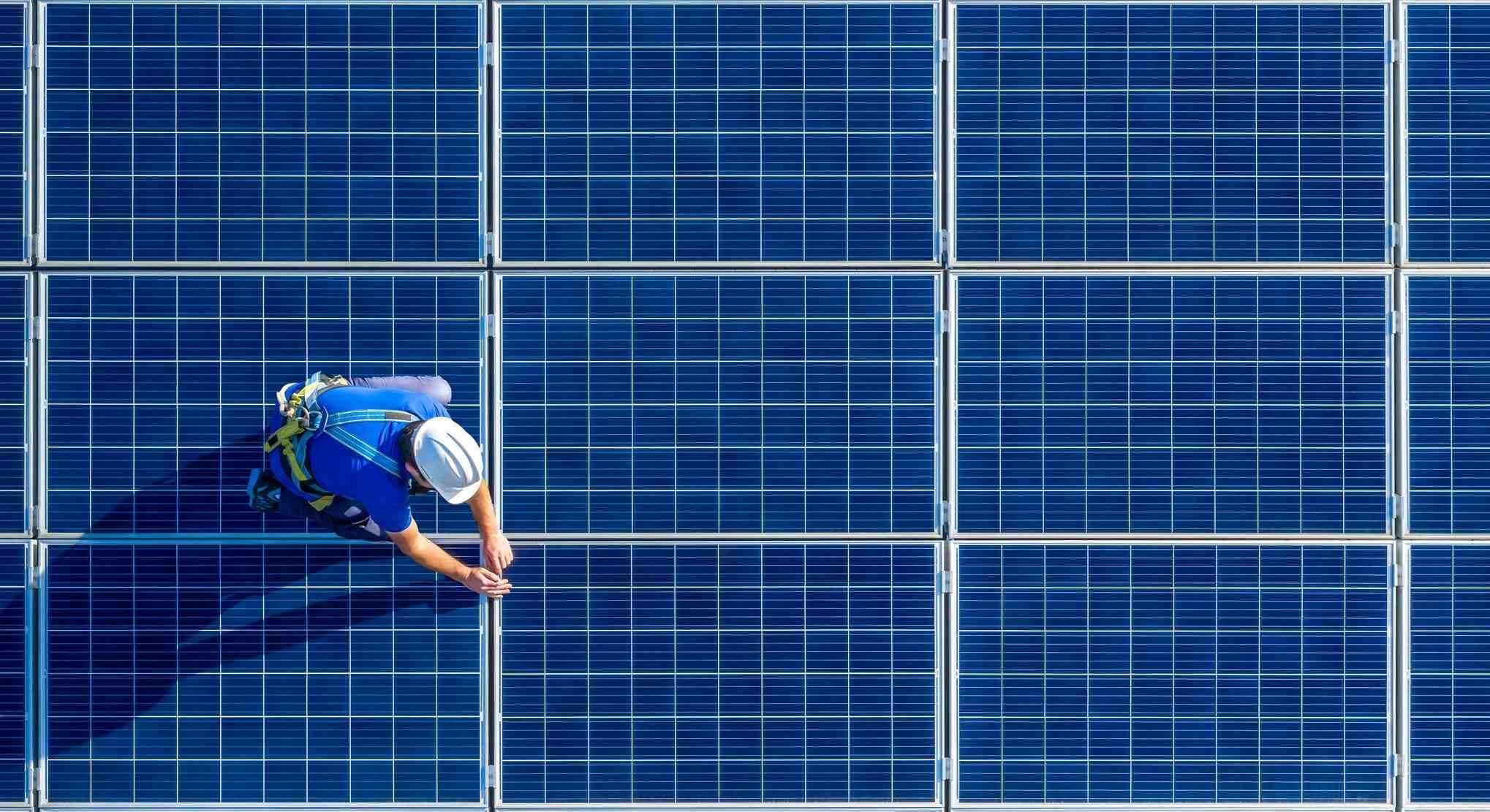 Photovoltaics Worker in safety gear installing blue solar panels in a rooftop array