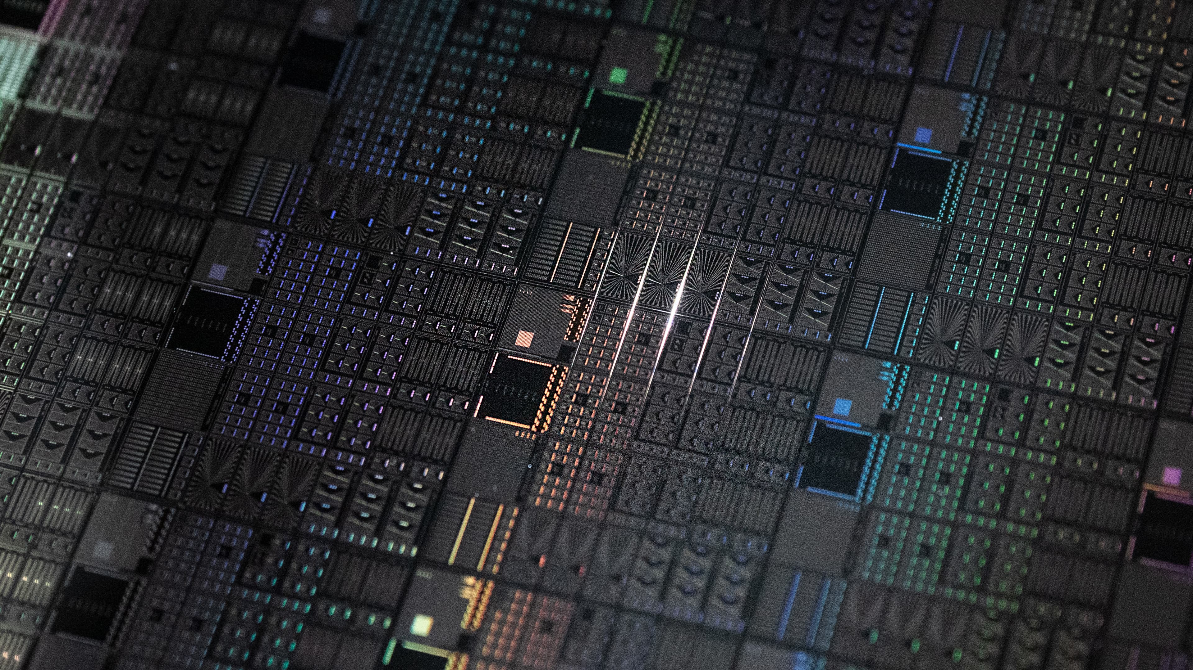 Physical%20spin%20qubits Close-up of a patterned semiconductor chip surface with colorful circuit structures.