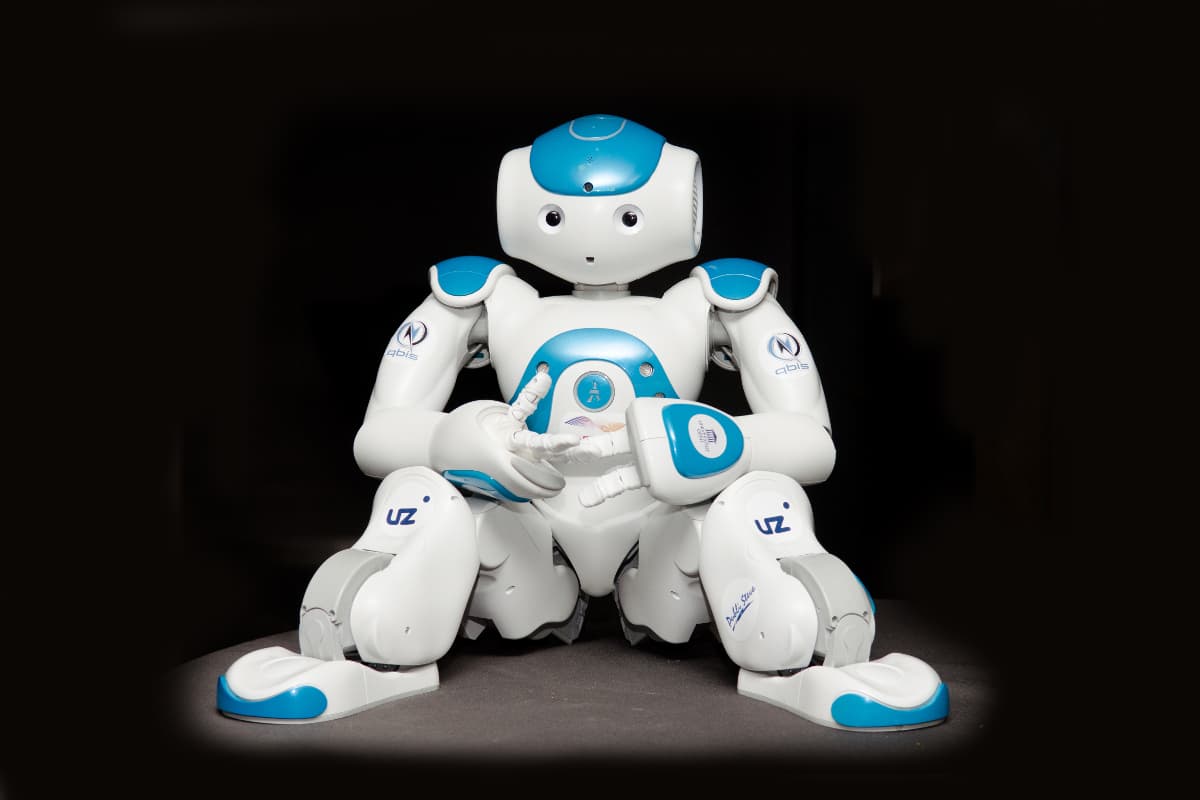 Zora humanoid robot sitting ready for care services Zora humanoid robot seated against a dark background, ready to provide care services