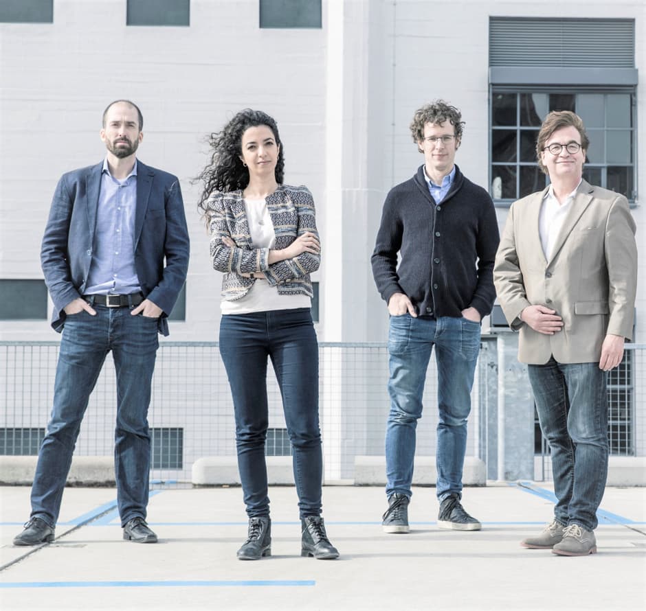 Four team members standing outdoors in front of building Four Onera team members stand outdoors in front of a building.