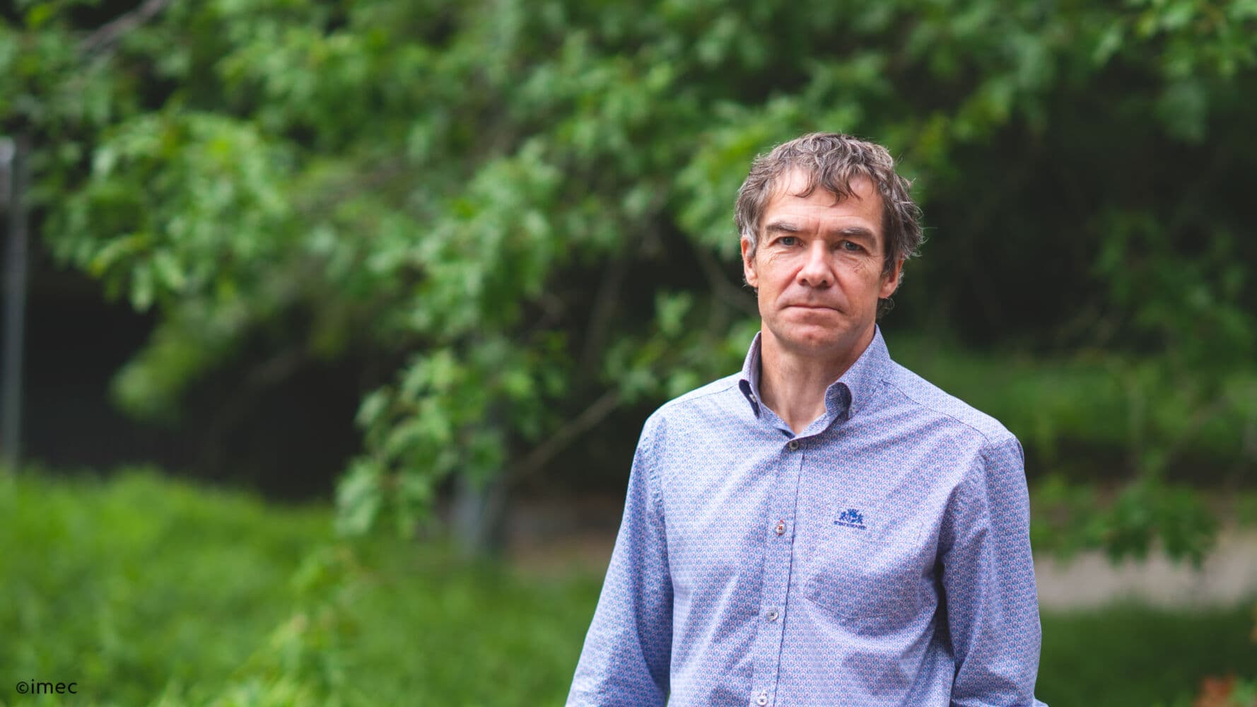 Piet-Wambacq Portrait of imec fellow Piet Wambacq standing outdoors against a green, blurred background.