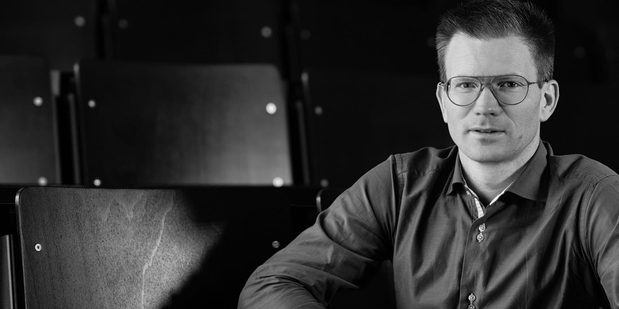 Pieter-Simoens001magazinenew_1 Black-and-white portrait of a man in glasses seated in an auditorium