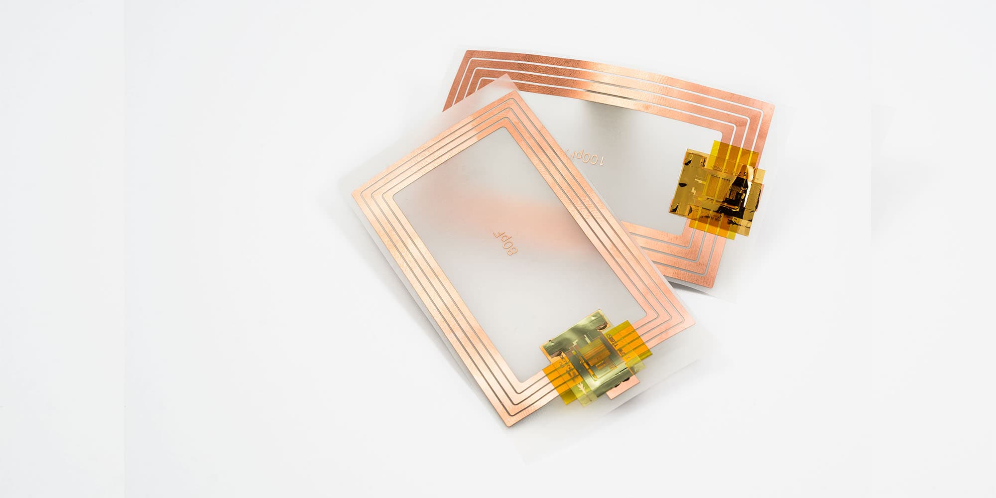 Plastic-NFC_1 Two rectangular plastic NFC tags with copper antenna traces and chip contacts on a white background