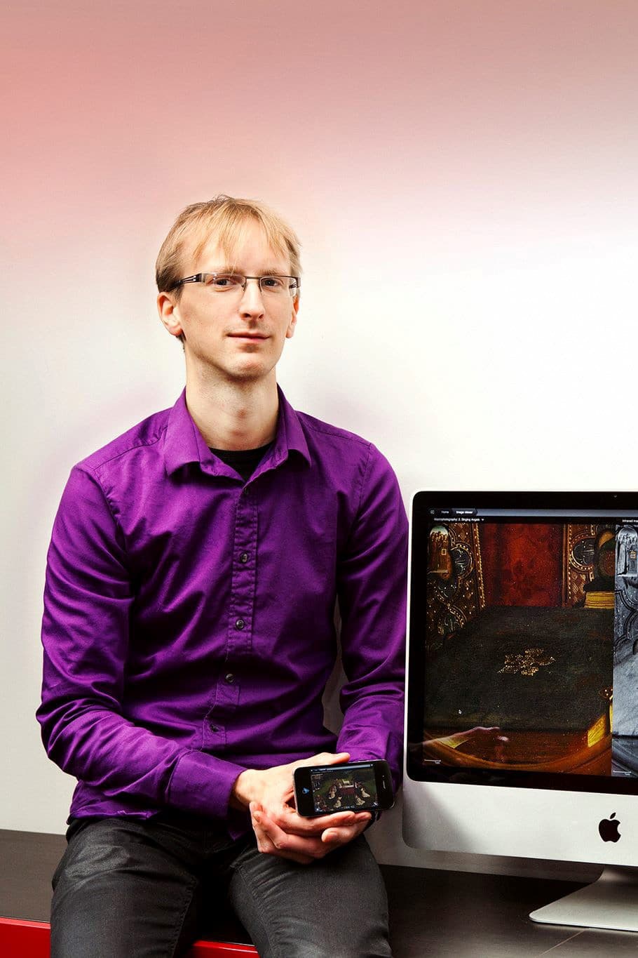 Portrait_Frederik_Temmermans_1 Frederik Temmermans zit naast een desktopmonitor en houdt een smartphone vast, met een digitaal kunstwerk op de schermen