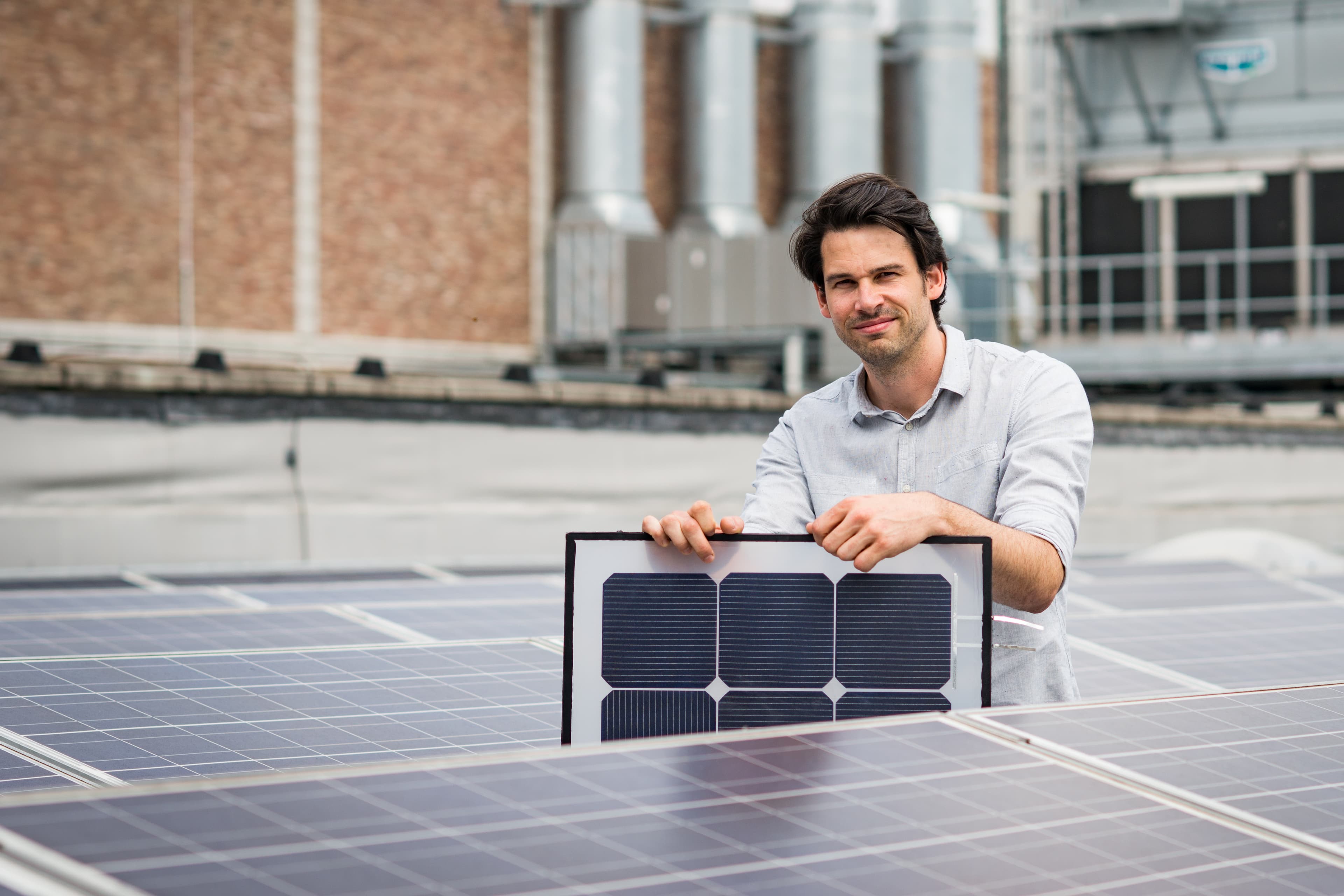 Press-release-energy-yield-calculation003_1 Man standing on a rooftop among solar panels, holding a framed photovoltaic cell
