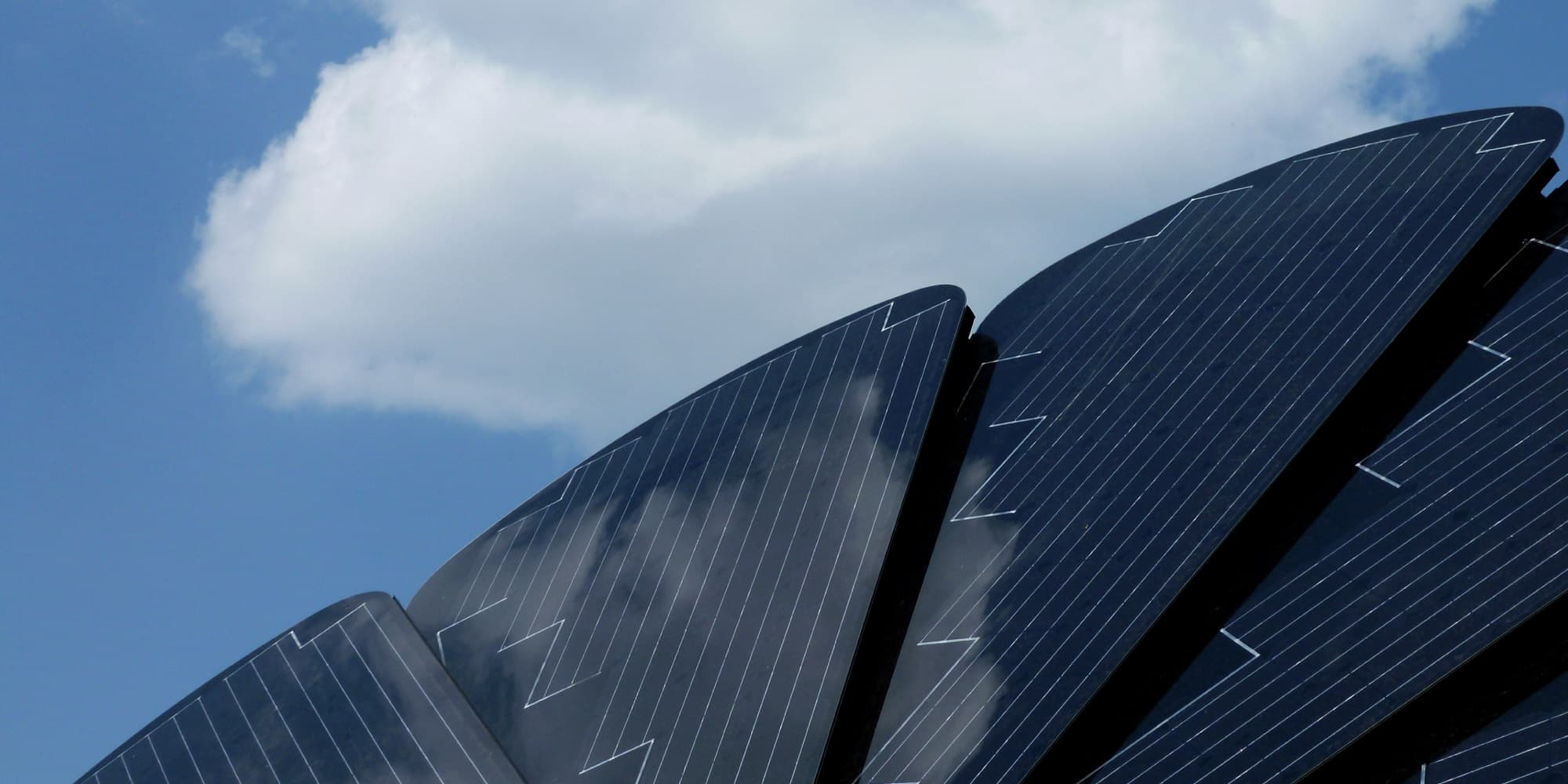 PV_header Curved thin-film solar panels against a blue sky with clouds