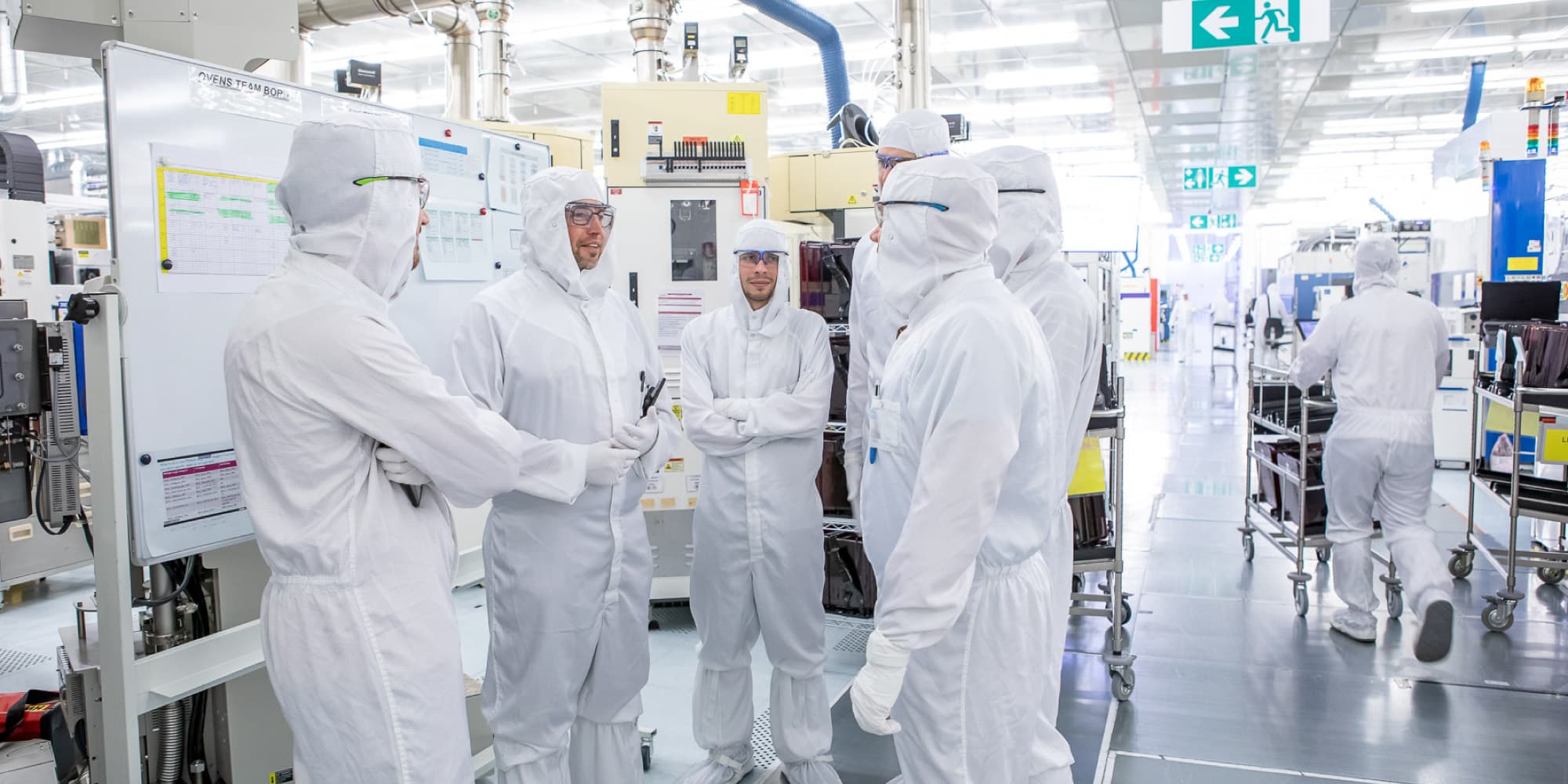 Research-and-development_1 Researchers in white cleanroom suits talking in a semiconductor lab with production equipment around them