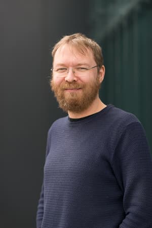 roel-wuyts_4 Portrait of Roel Wuyts, a bearded man wearing glasses and a dark sweater against a blurred background.