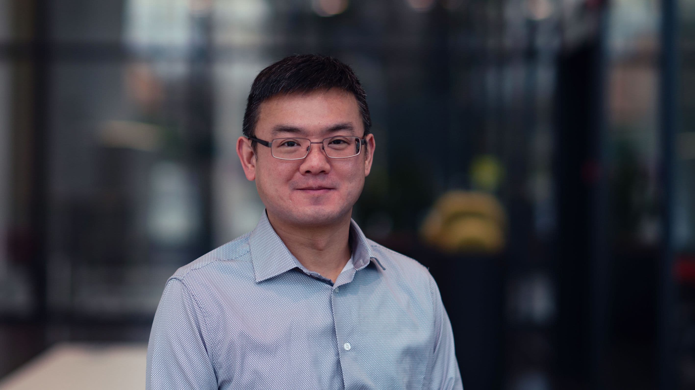 Shih-Hung%20Chen Portrait of Shih-Hung Chen in a light blue shirt and glasses, standing in a blurred indoor lab setting.