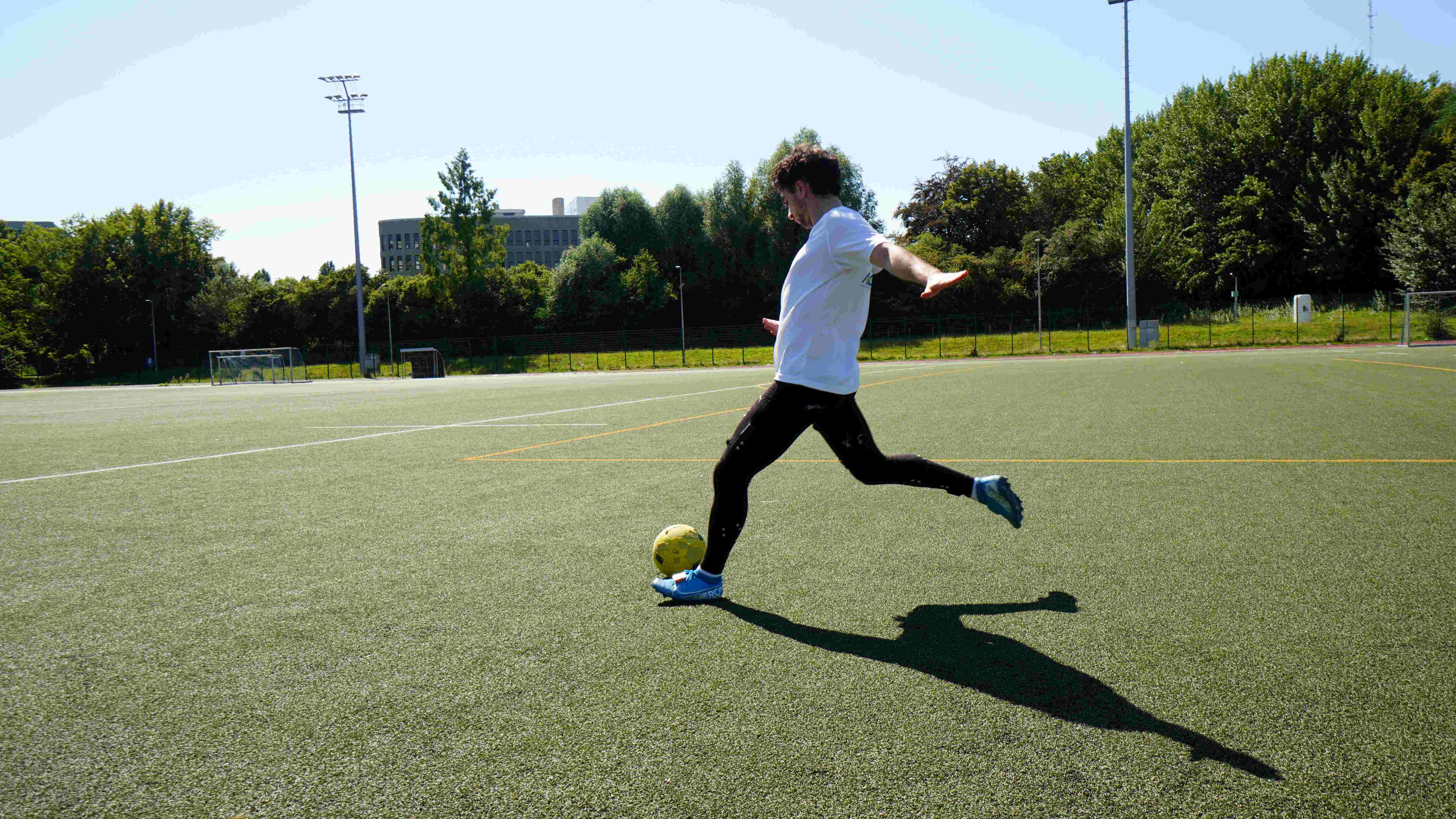 Skinetixsportswear Atleet in sportkleding met sensoren die een voetbal schopt op een buitenterrein