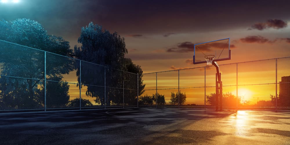 smart-lightning-basketveld Leeg basketbalveld buiten bij zonsondergang achter een omheinde slimme verlichtingsinstallatie