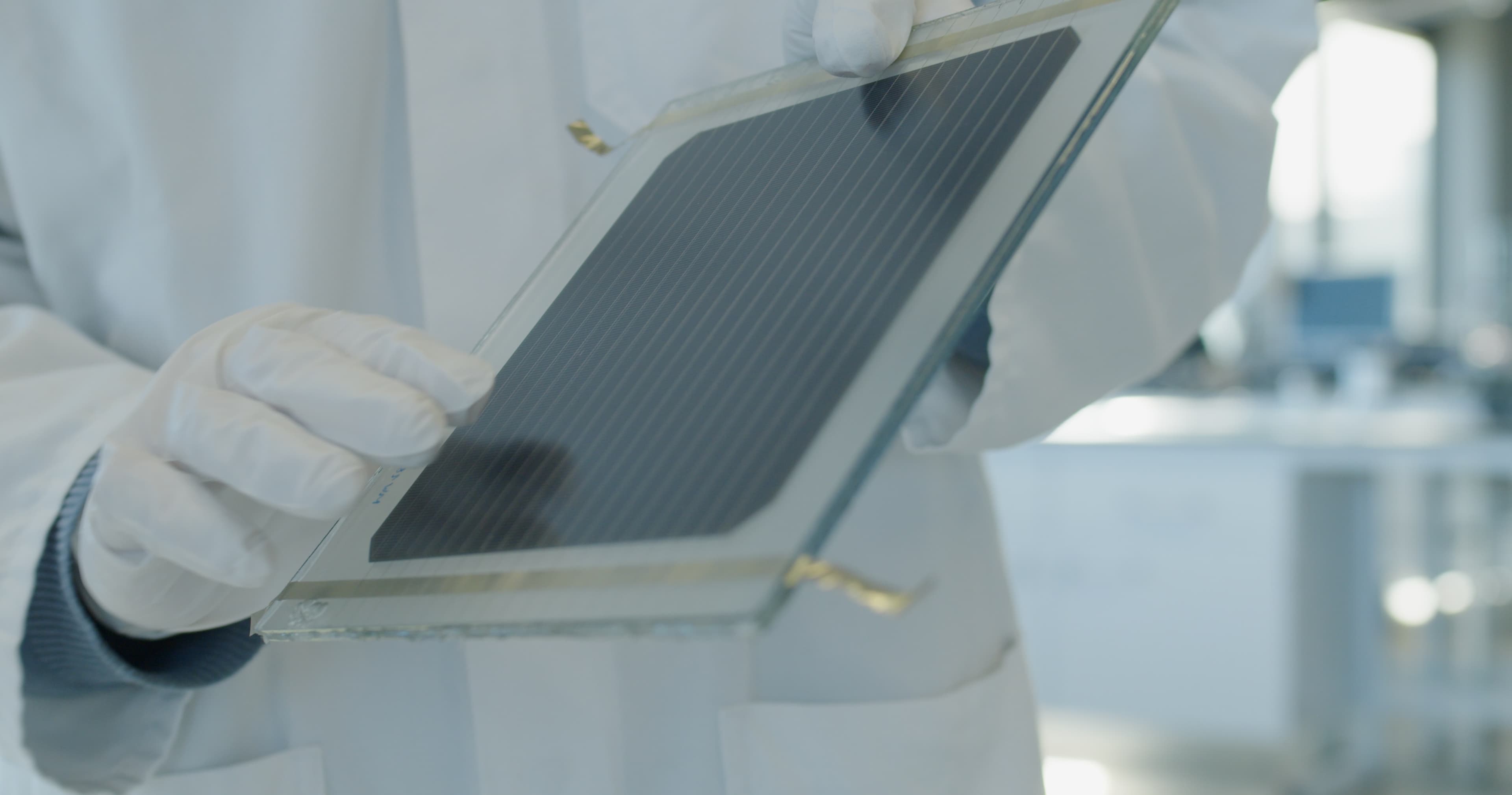 SNROOF_zonnepaneel_03 Gloved hands hold a curved glass solar panel with a dark photovoltaic cell inside a clean lab
