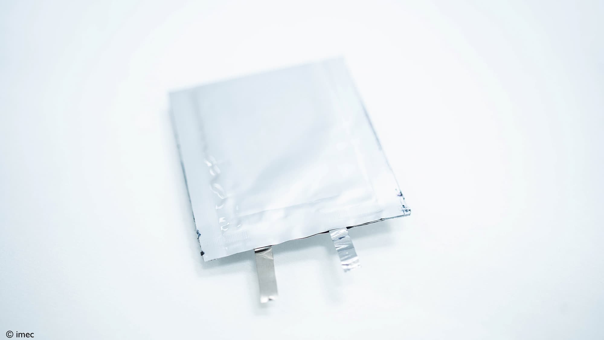 SOLiDIFY-1020-Wh-L-solid-state-battery_resize Transparante prototype solid-state batterij-pouchcel met twee metalen tabs op een witte achtergrond.