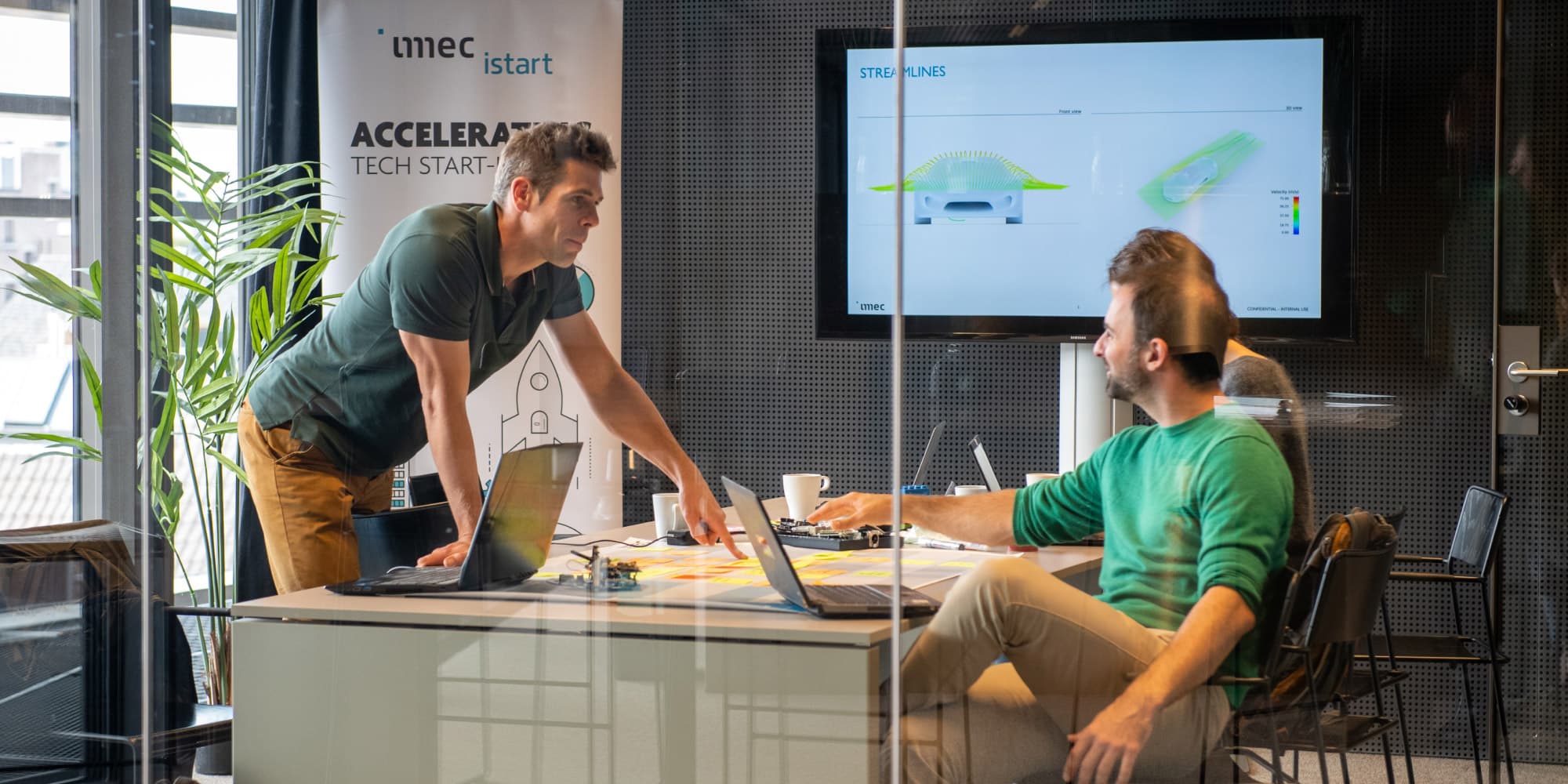 Start-up Two entrepreneurs discuss a startup project in an imec.istart meeting room with laptops and a presentation screen.