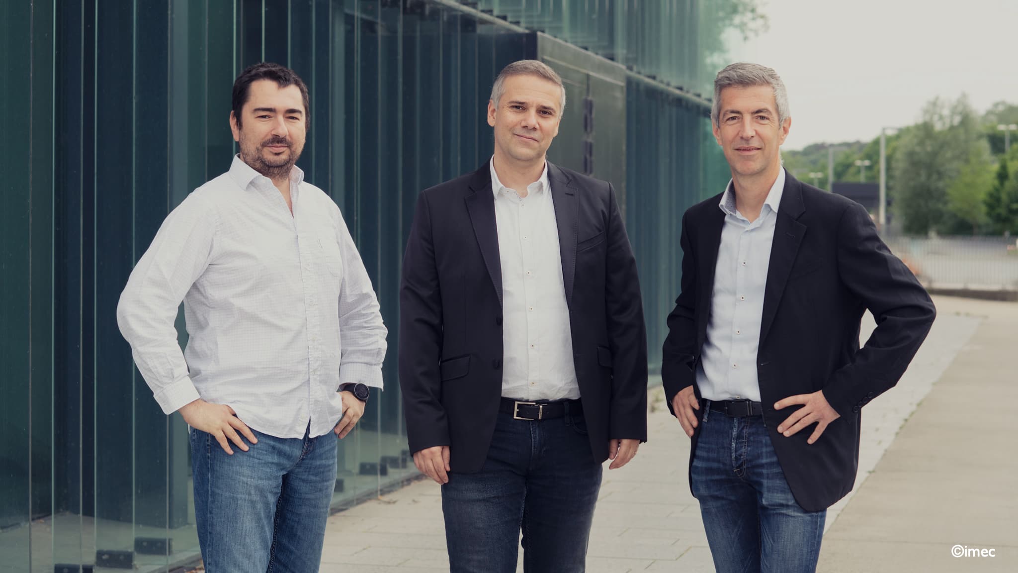 Swave%20headshot Three men in business attire posing outdoors beside a modern glass building
