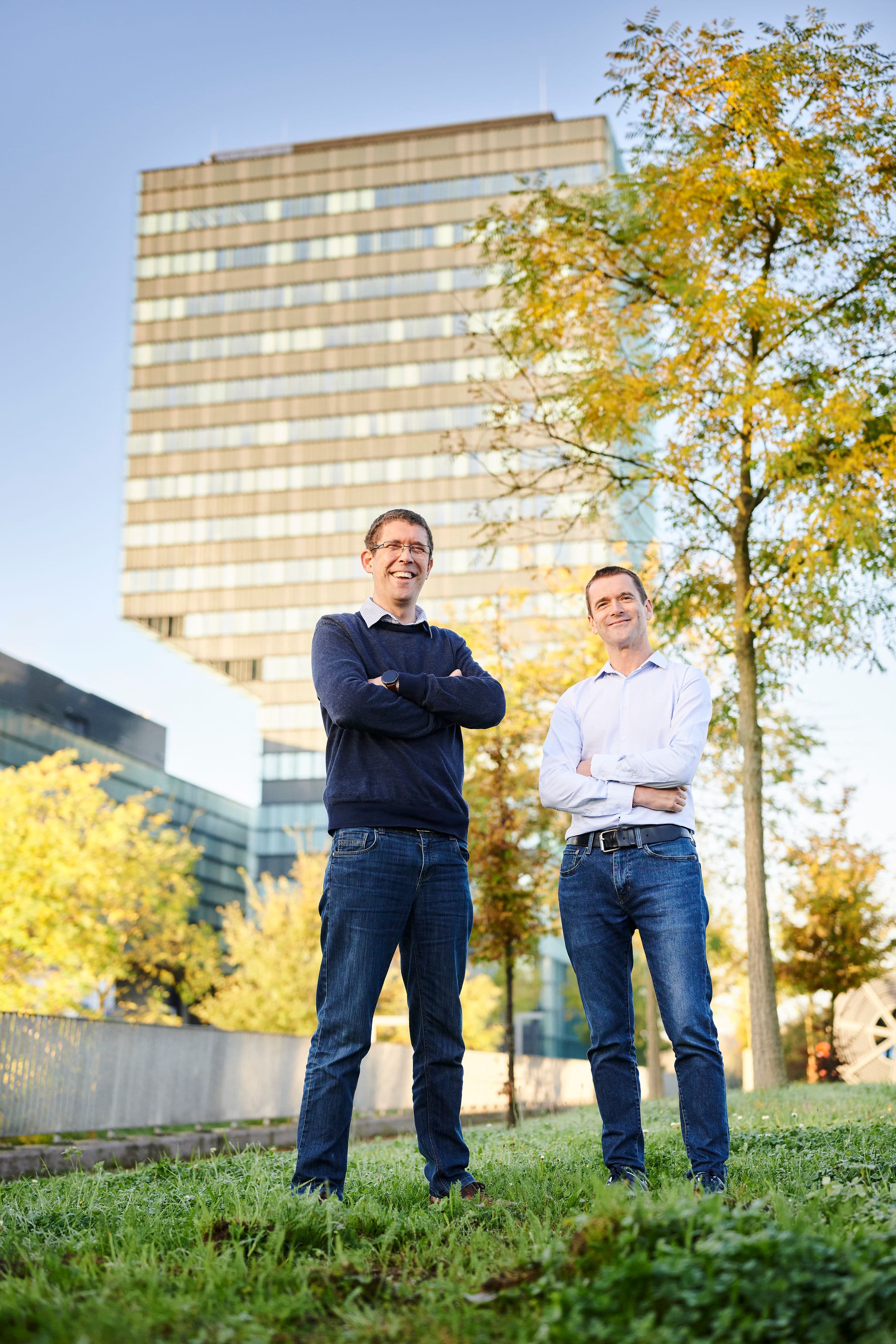 Sylvain%20Dubois%20Sebastien%20Couet%20Vertical%20Compute%20imec%20tower Two men stand with arms crossed in front of an office building and autumn trees