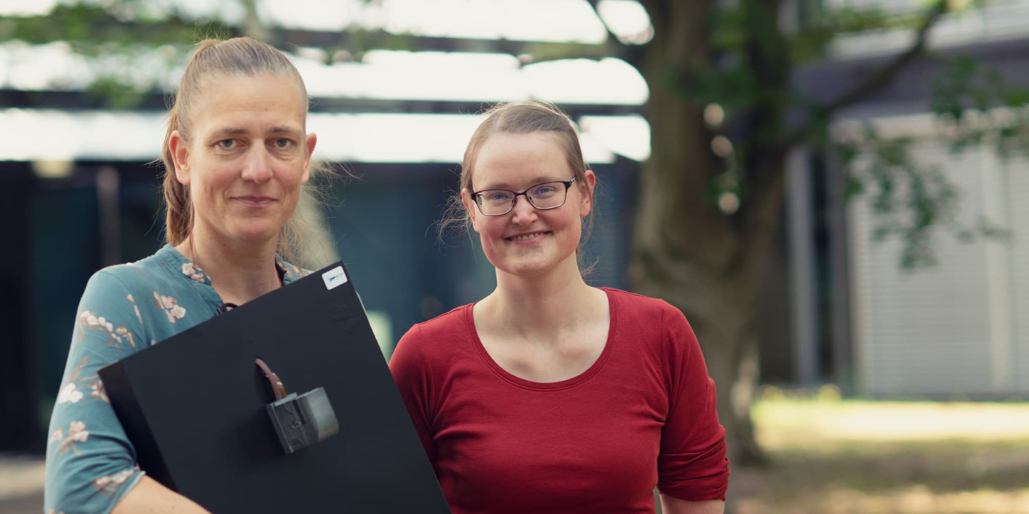 technical-pride-Measuring-blood-oxygen-levels-using-integrated-photonics Two women outdoors holding a black sensor prototype, smiling at the camera.