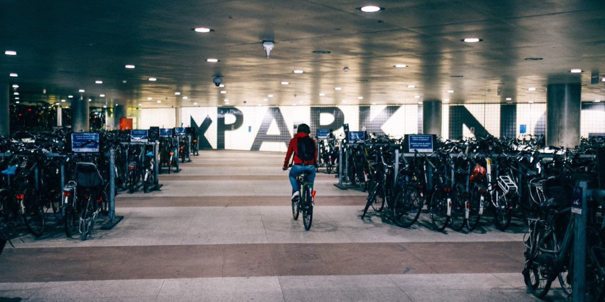 Tegen-2026-wordt-fietsen-comfortabeler-en-veiliger-dankzij-inzichten-uit-data-spaces. Fietser die door een ondergrondse fietsenstalling rijdt, met rijen fietsen