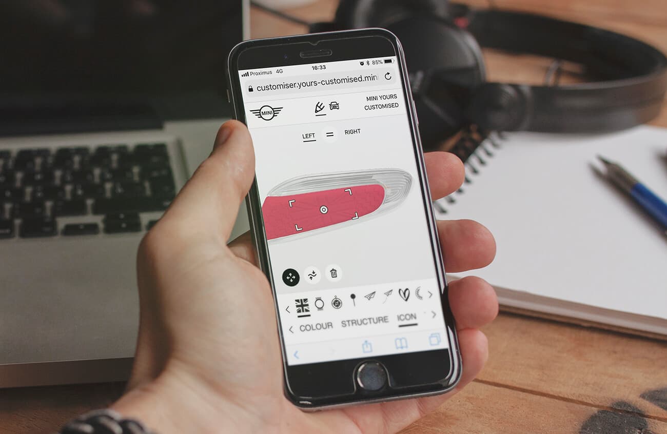 Twikit_Mockup_customers-1 Hand die een smartphone vasthoudt met de Twikbot-interface voor het aanpassen van een MINI-autoonderdeel