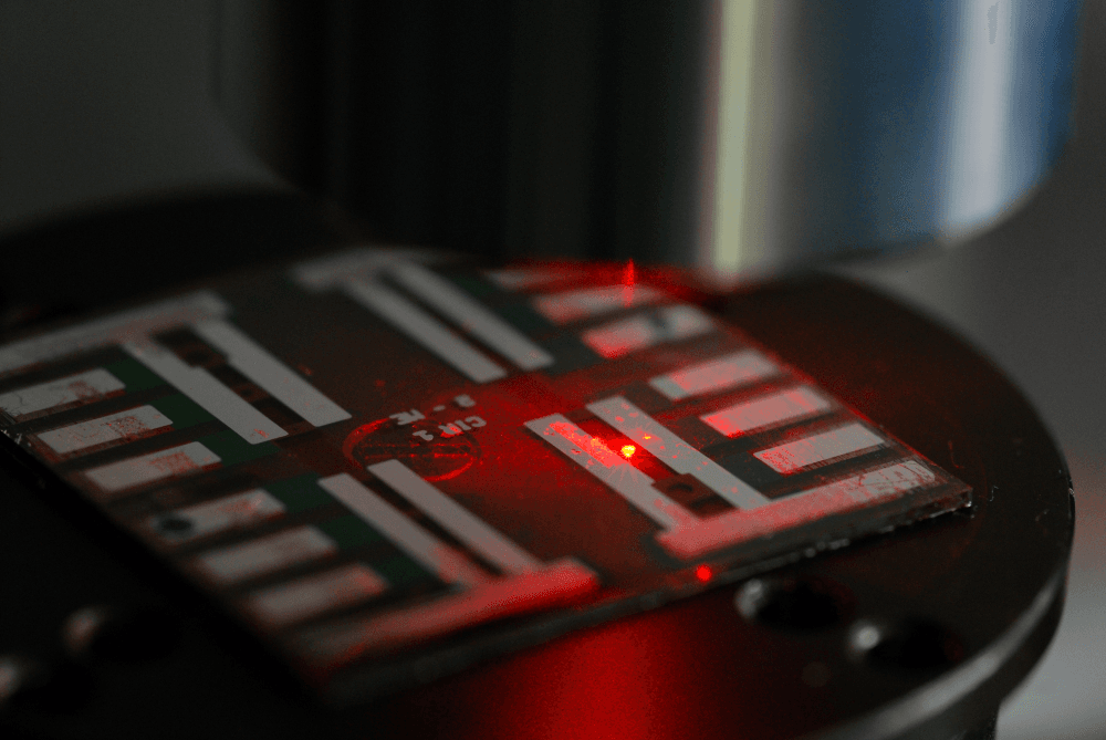 ULTRALUX Perovskite LED chip glowing red under test on a microscope stage
