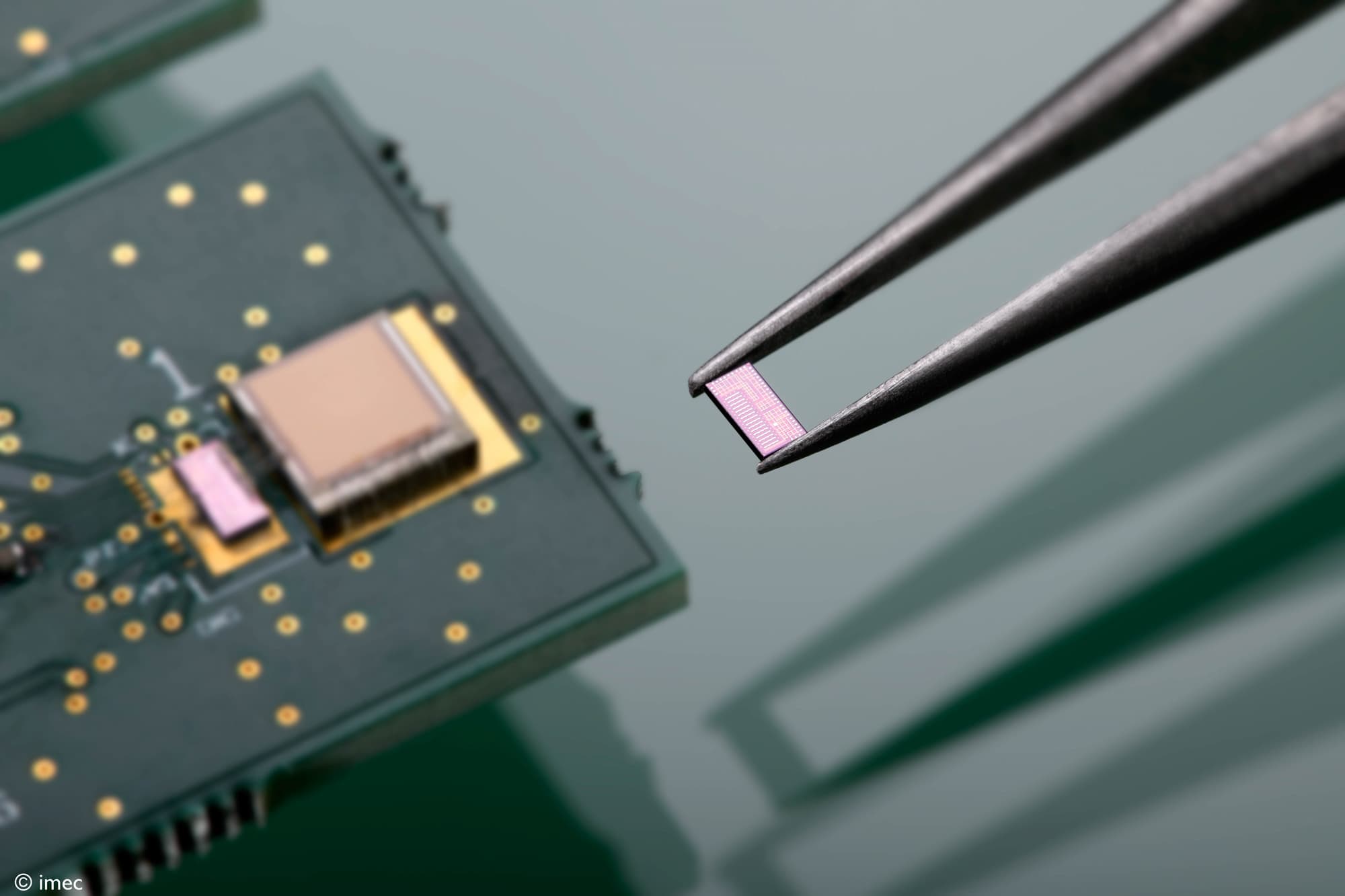 Ultrasound-powering-resize Een pincet houdt een kleine roze chip voor draadloze voeding boven een printplaat