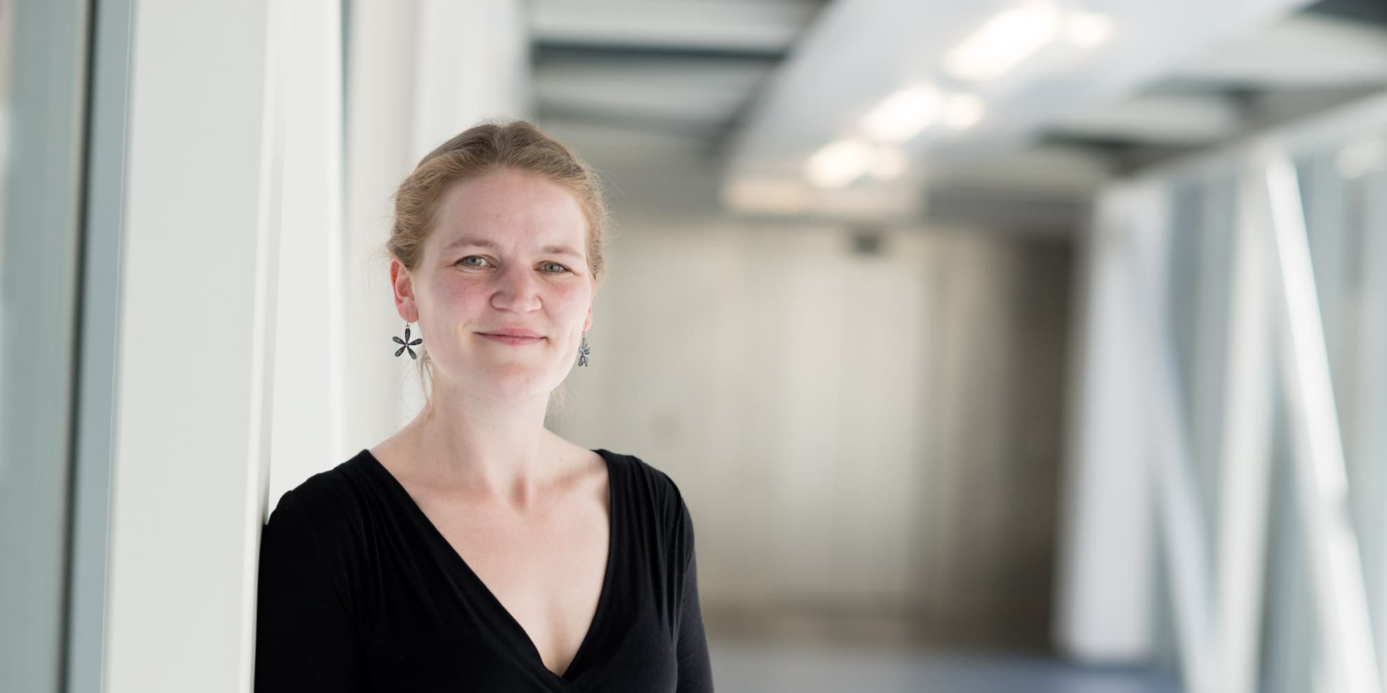 veerle_1 Veerle Reumers standing in a bright corridor, wearing a black top and flower-shaped earrings
