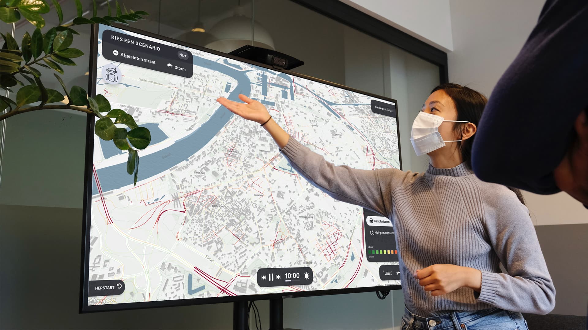 visual_Digitaltwin%28dubai%29_verkeerstromen_bgscreen Vrouw met een masker wijst naar een grote digitale stadskaart met verkeersscenario's