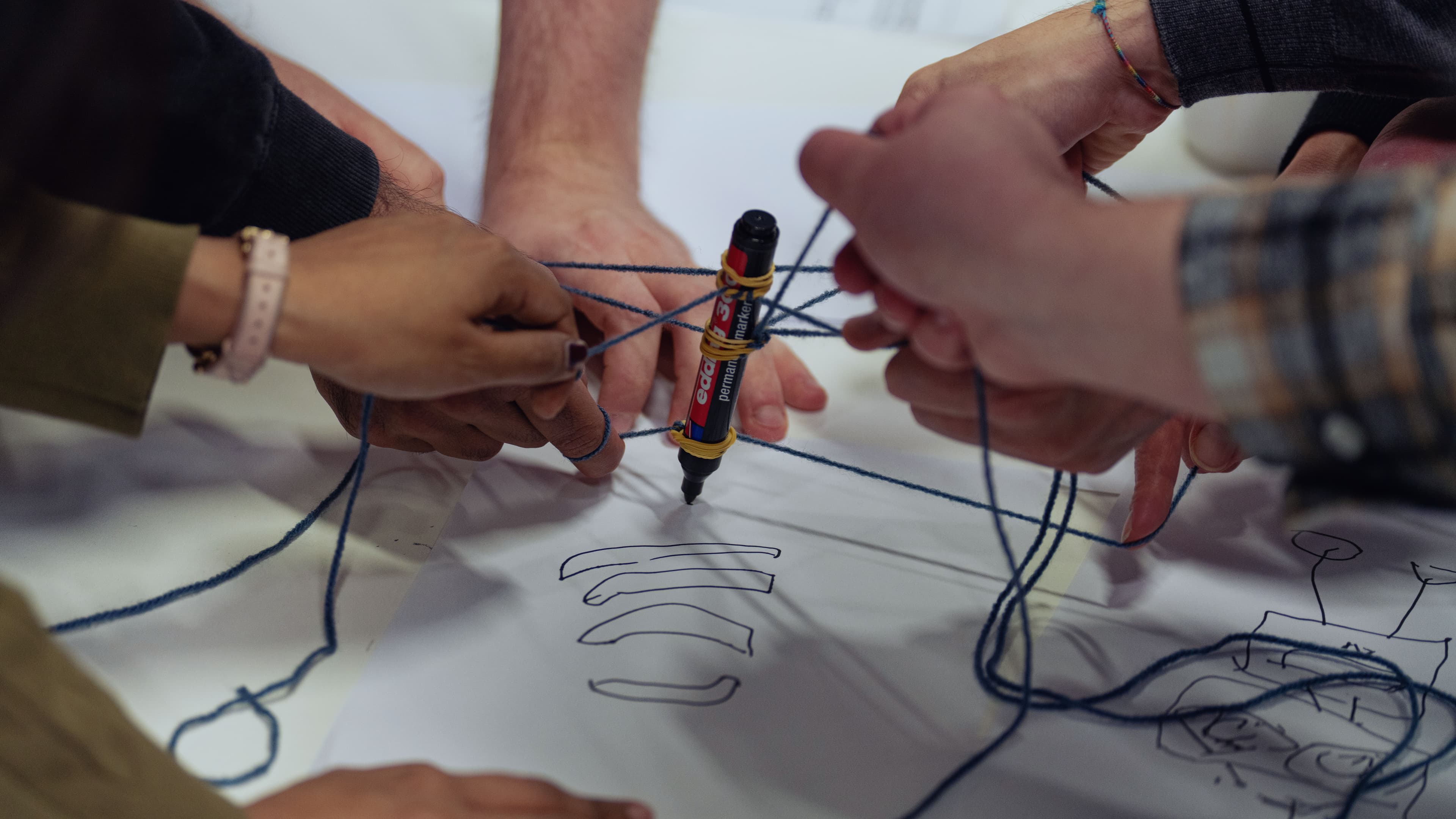 We%20care%20about%20the%20difference%20you%20make Hands working together to connect strings around a marker on a paper sketch
