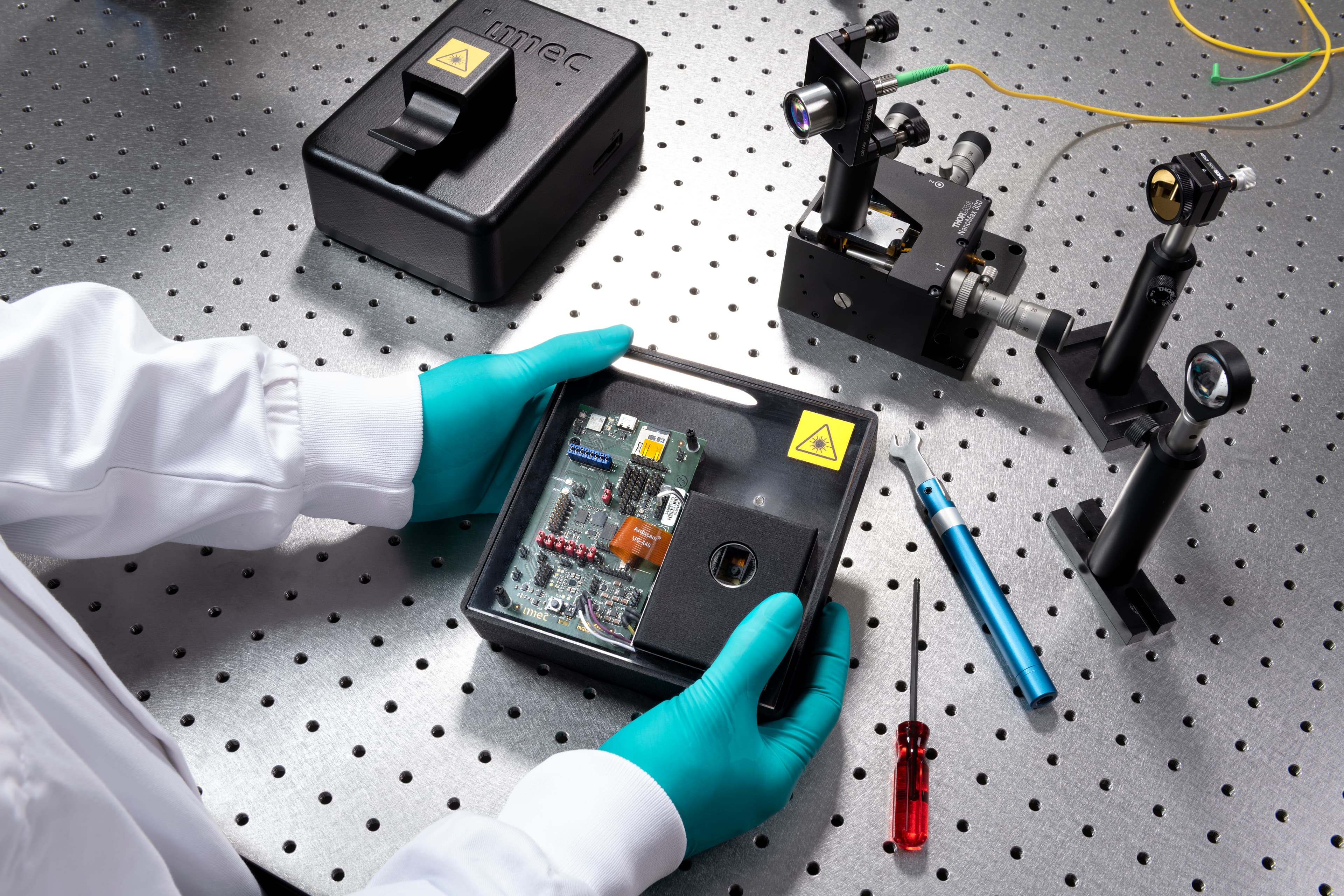 Wearable%20speckle%20sensing%20by%20imec Gloved researcher handling a wearable speckle sensing device on an optical lab bench with laser equipment