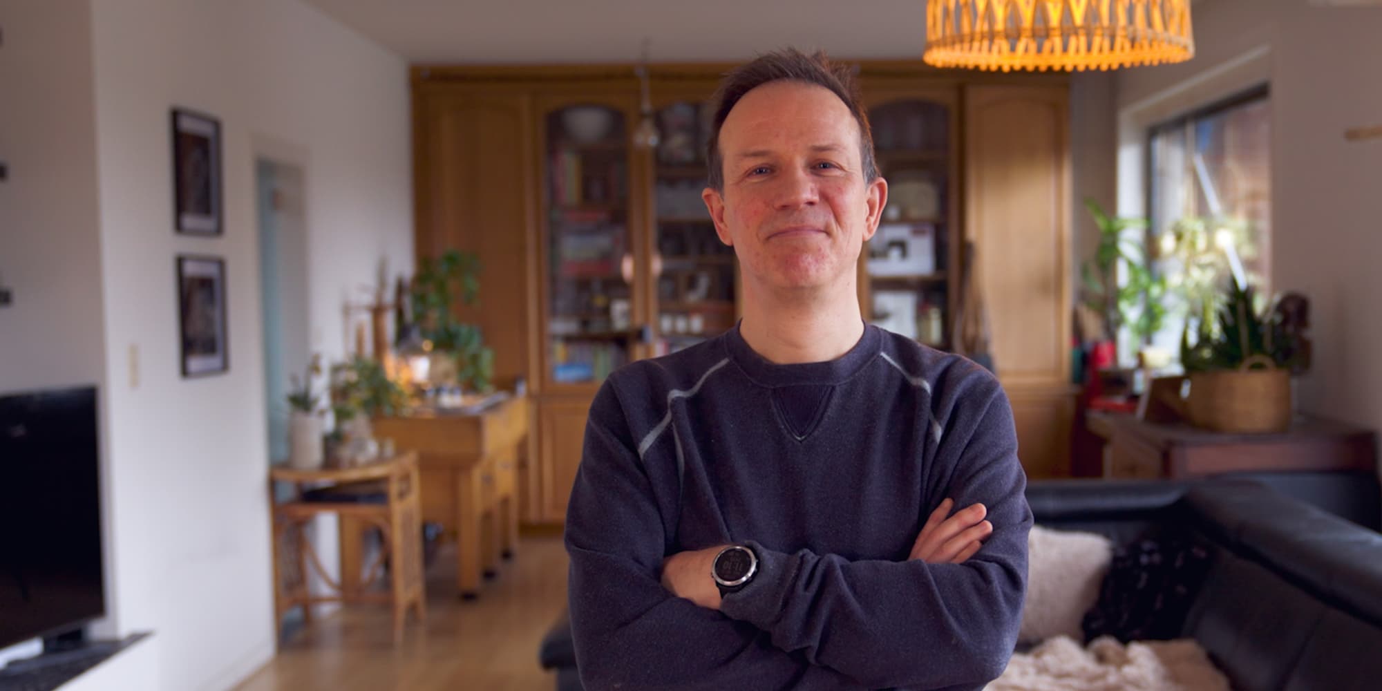 Wim-Fyen Man staat met de armen over elkaar in een warme woonkamer en kijkt naar de camera