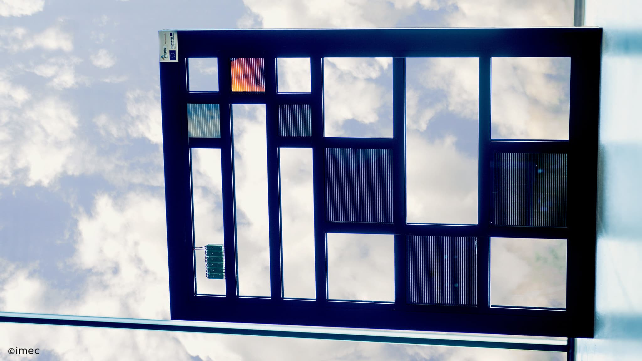 Window-integrated%20thin-film%20PV Window-integrated thin-film solar panel with colored photovoltaic cells against a cloudy sky