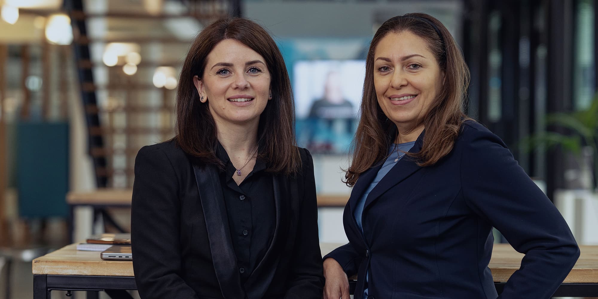 Womens-day Two women in business attire smiling in an office setting