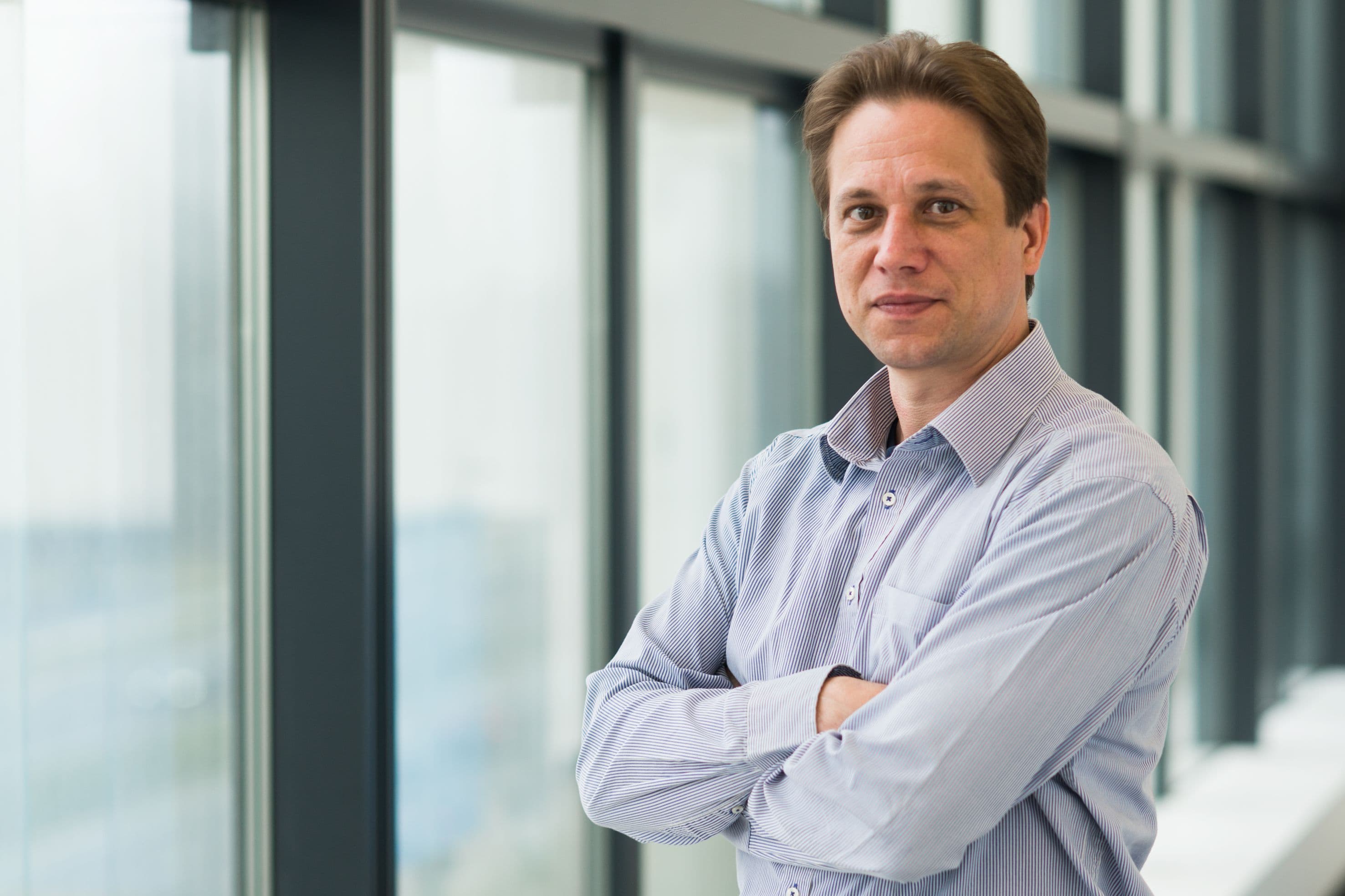 Zsolt_Tokei_1 Portrait of Zsolt Tokei standing with arms crossed in front of large office windows