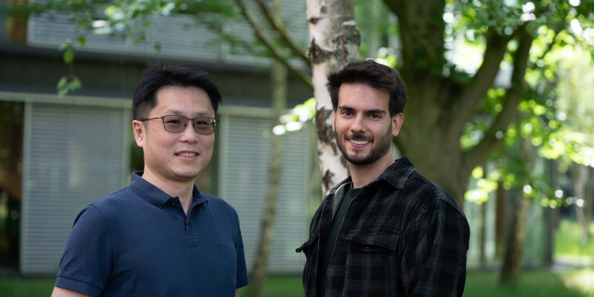 From-curiosity-to-impact-A-PhD-journey-at-imec Two smiling PhD students standing outdoors in front of a building and trees.