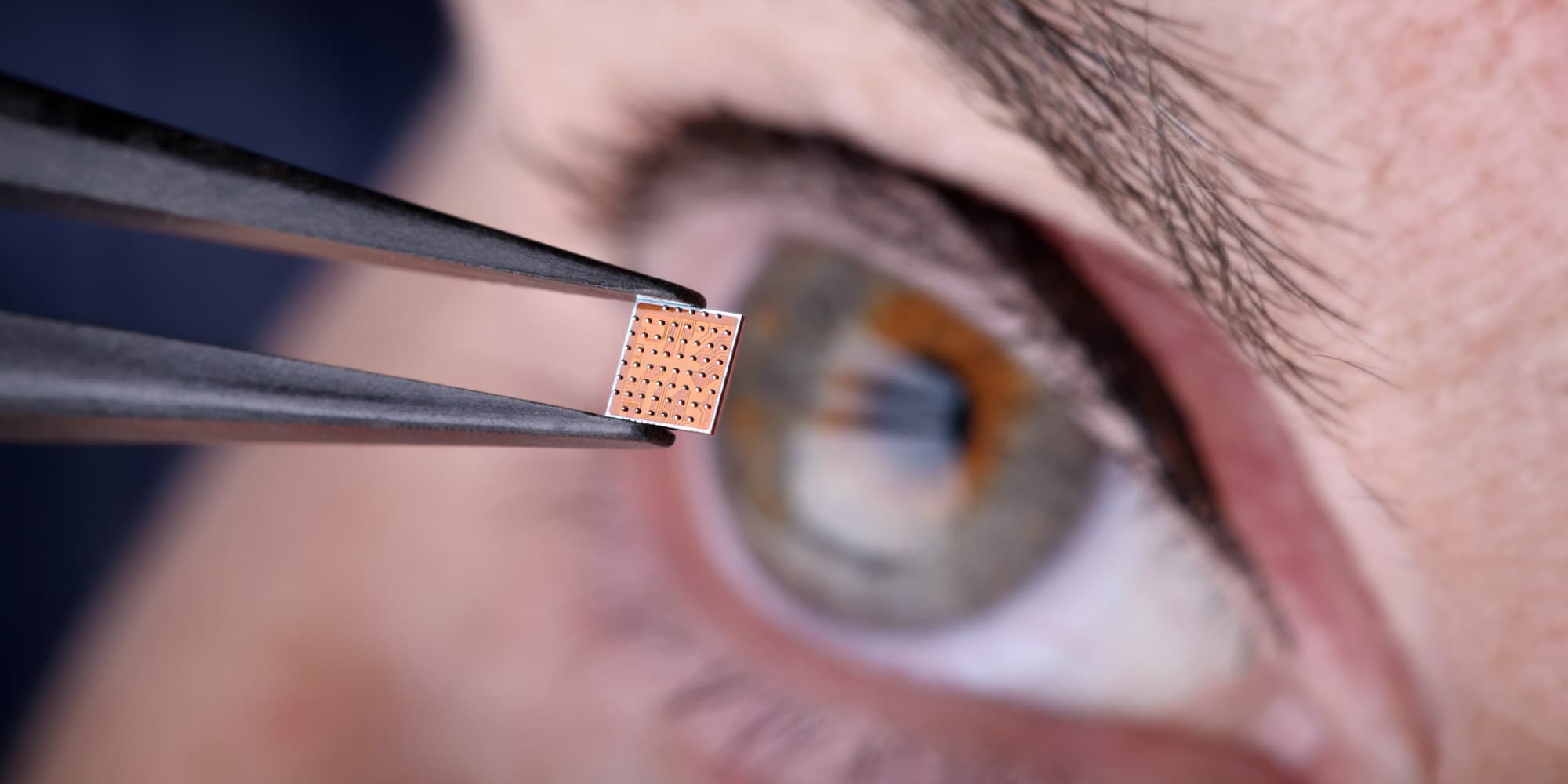 Header-imec-NL-2026 Tweezers hold a small microchip in front of a close-up eye