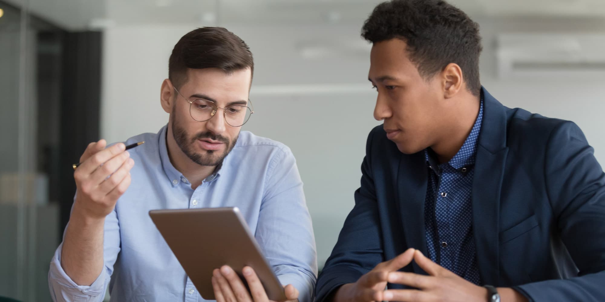 sales-management-support Two colleagues review a tablet during a business discussion.