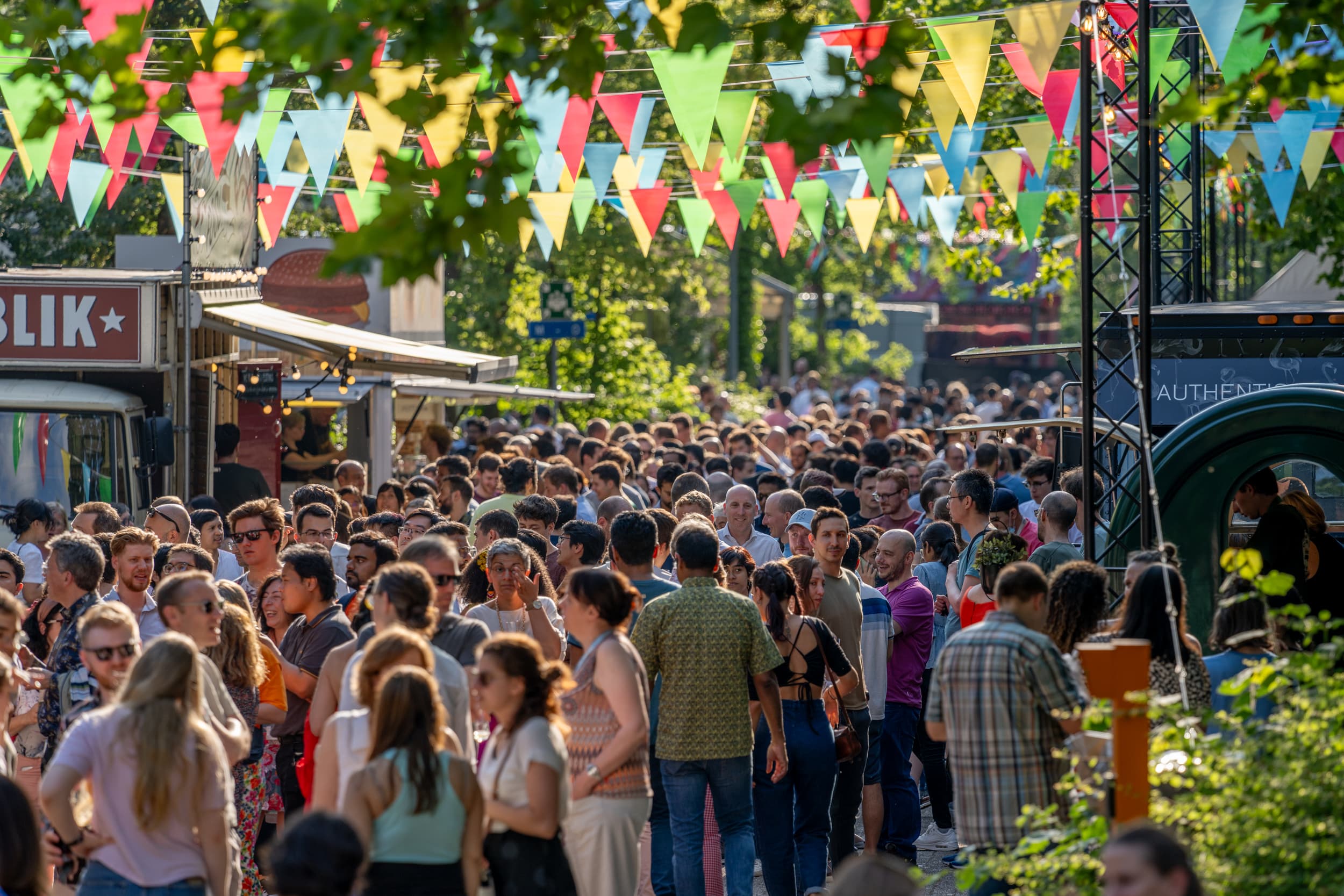 Summer%20festival%20202300097 Crowd at an outdoor summer festival with colorful bunting strung overhead