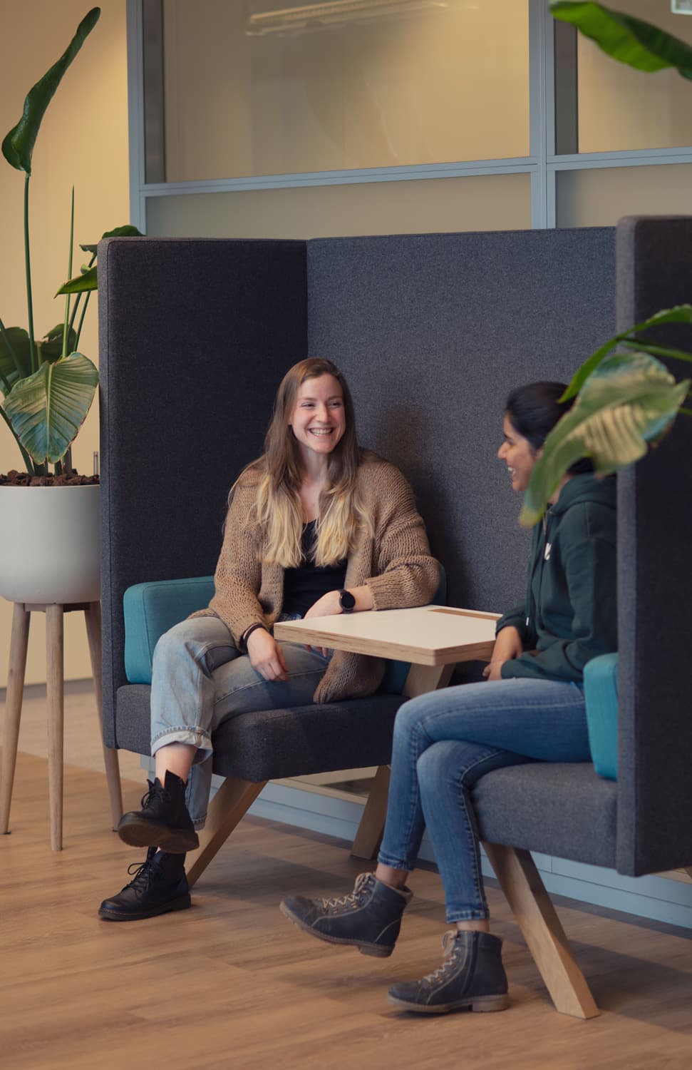 time Two women chatting in a quiet lounge seating area with plants and a small table