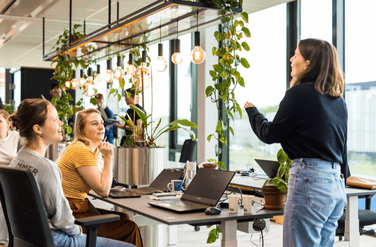 WPVH Students and a presenter in a bright office workspace with laptops and hanging plants