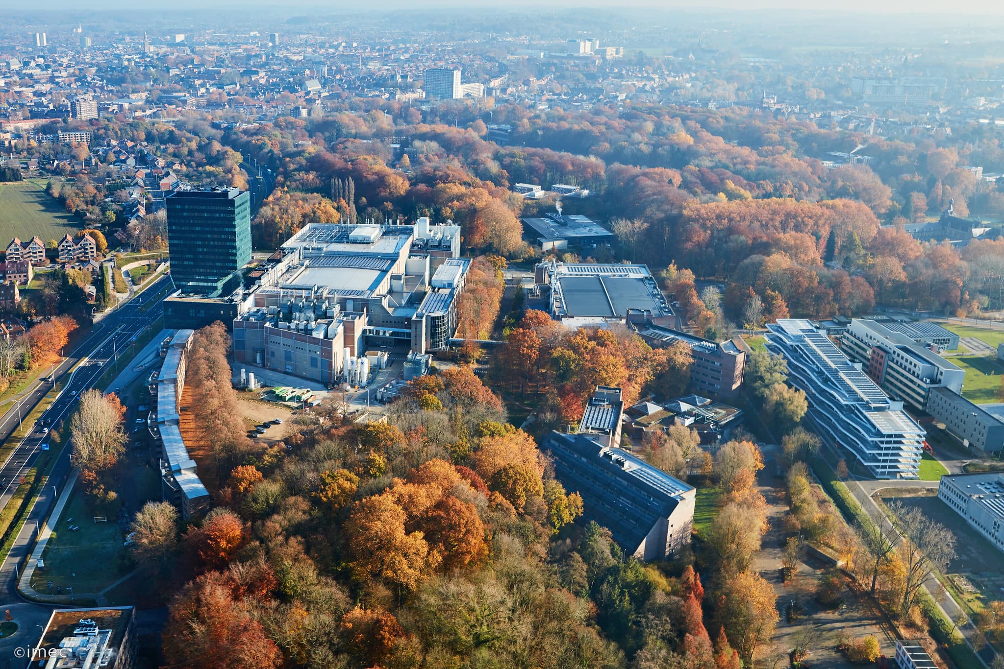 imec%20Leuven%20sky Aerial view of imec's Leuven campus surrounded by autumn trees and city buildings