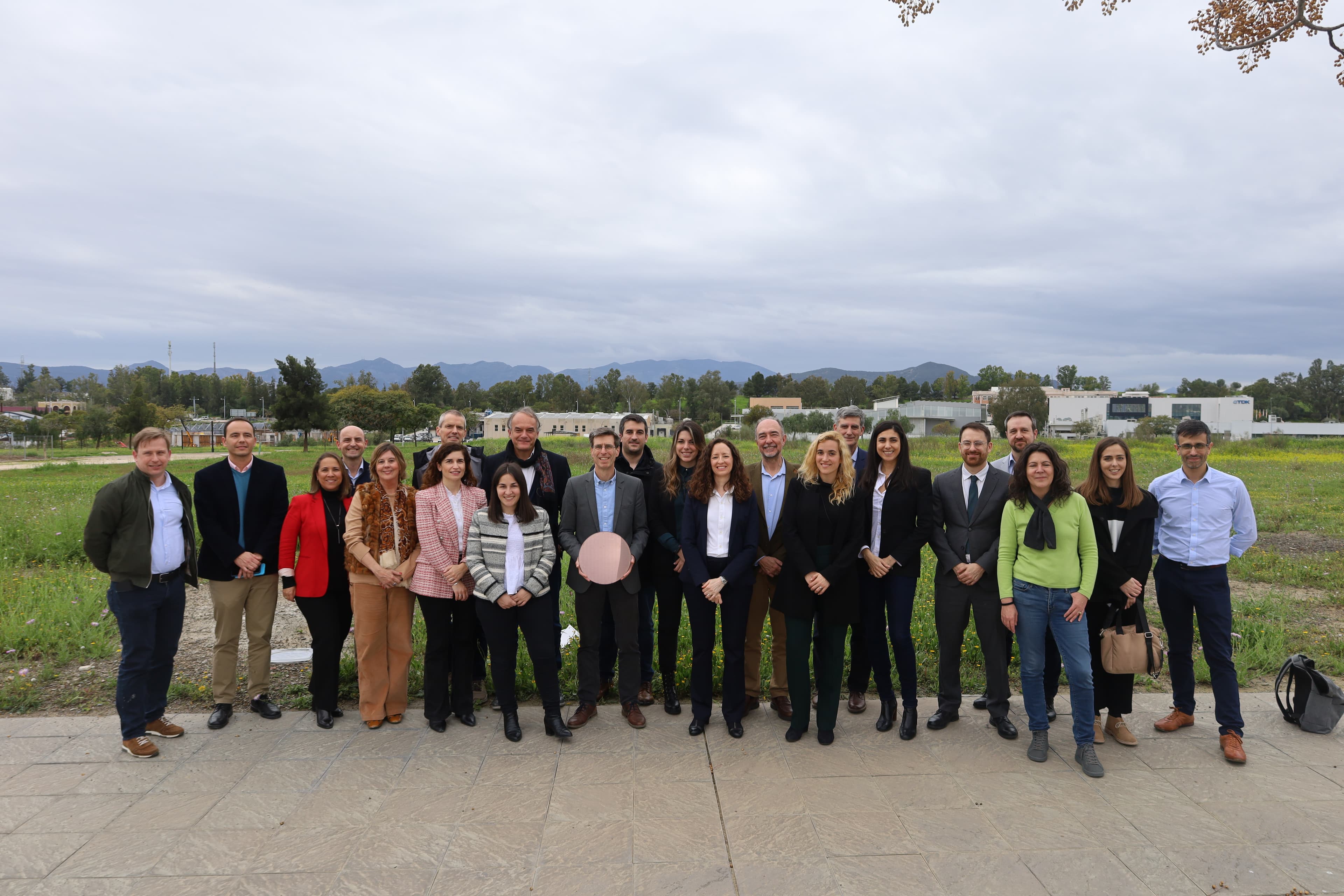 Group photo outdoors in front of imec buildings Group of people posing outdoors in front of imec buildings and a landscape, with mountains in the distance.